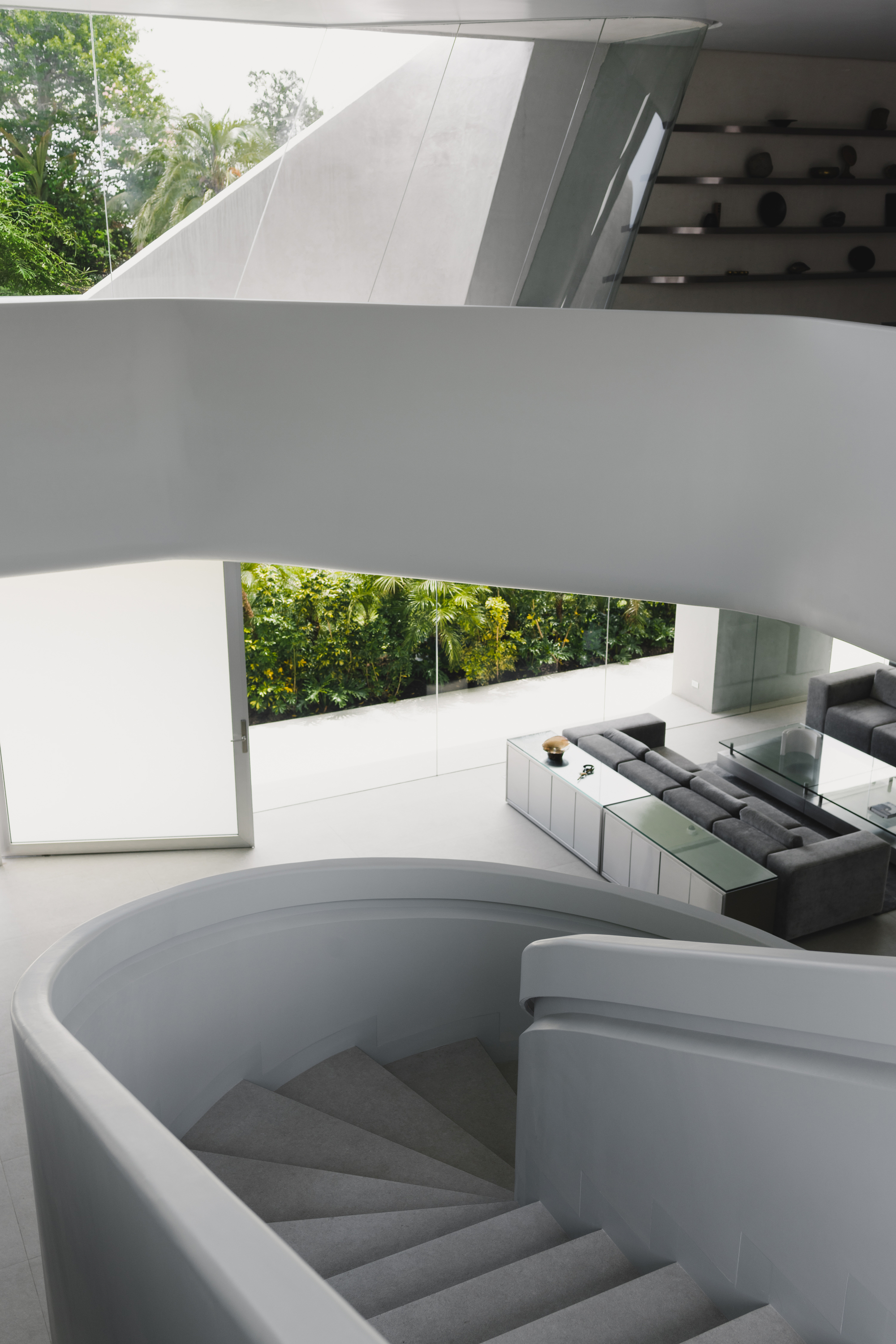 Curved concrete staircase descending beneath a sculptural white overhang with trees visible beyond