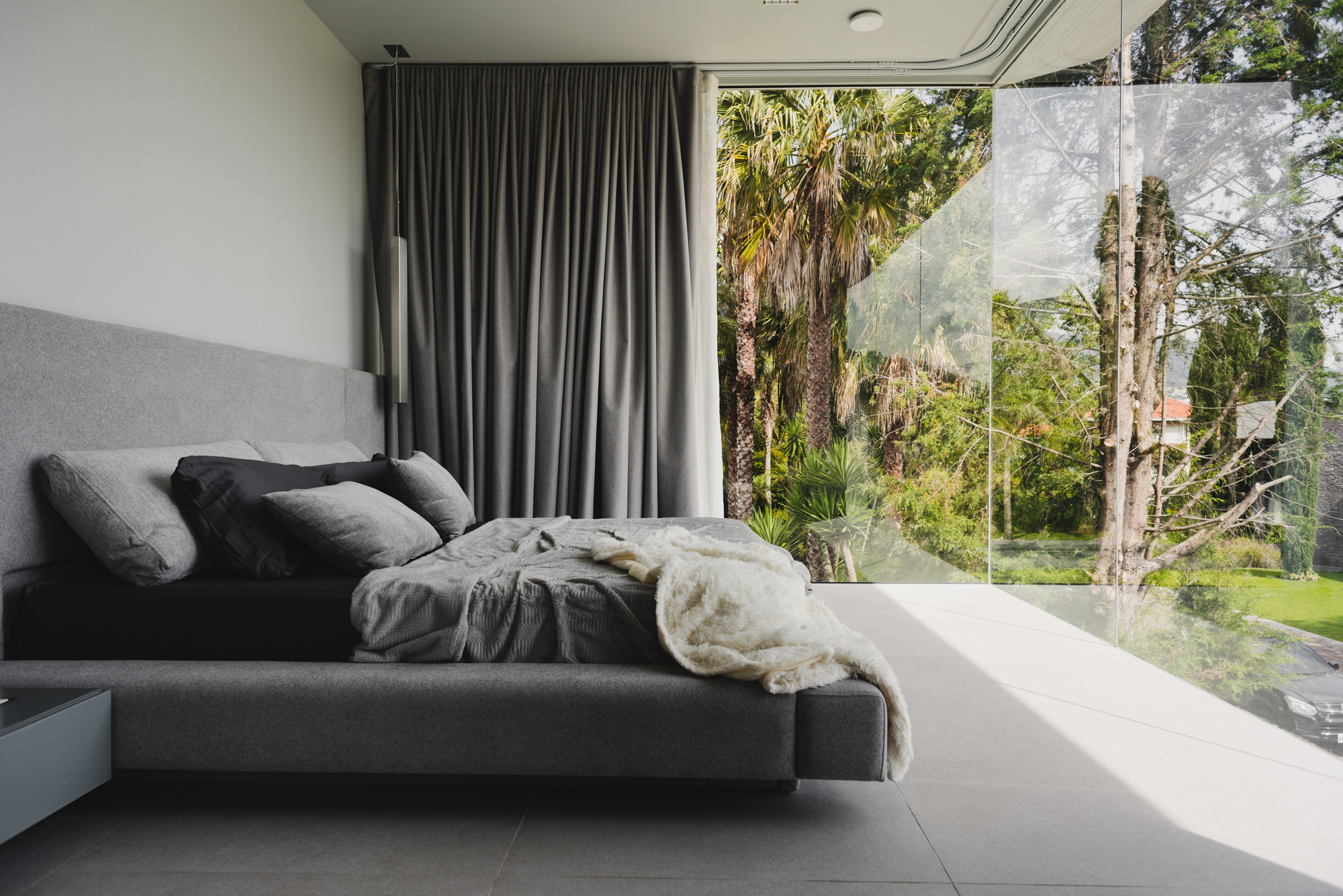 Bedroom with full-height glazing framing views of palms and tropical vegetation outside