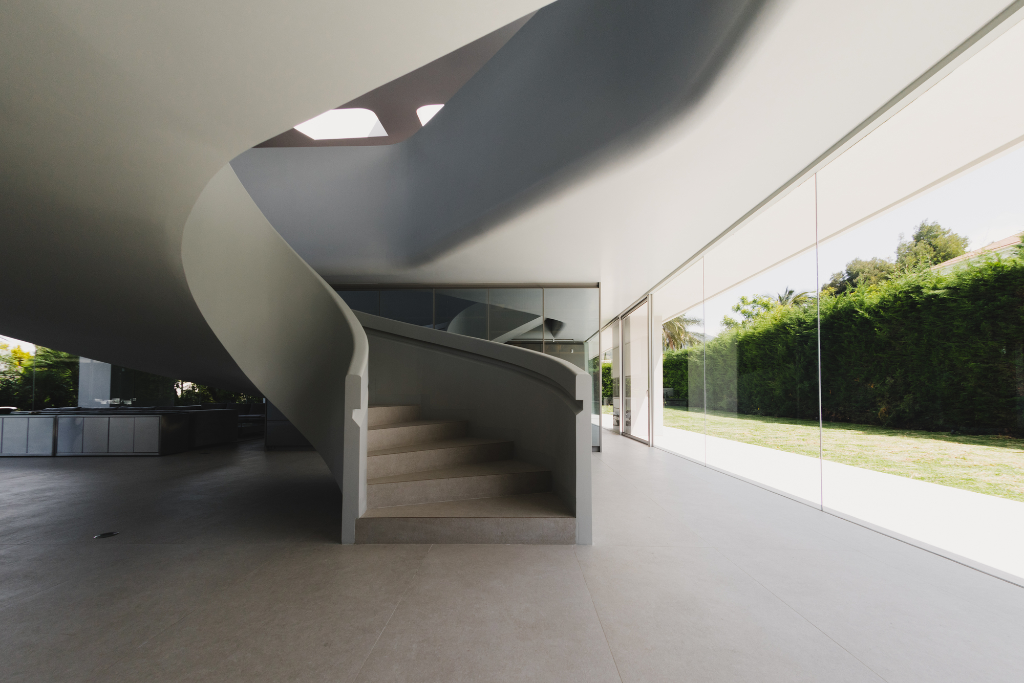 Helical staircase with concrete treads winding upward beside the glazed wall facing the garden