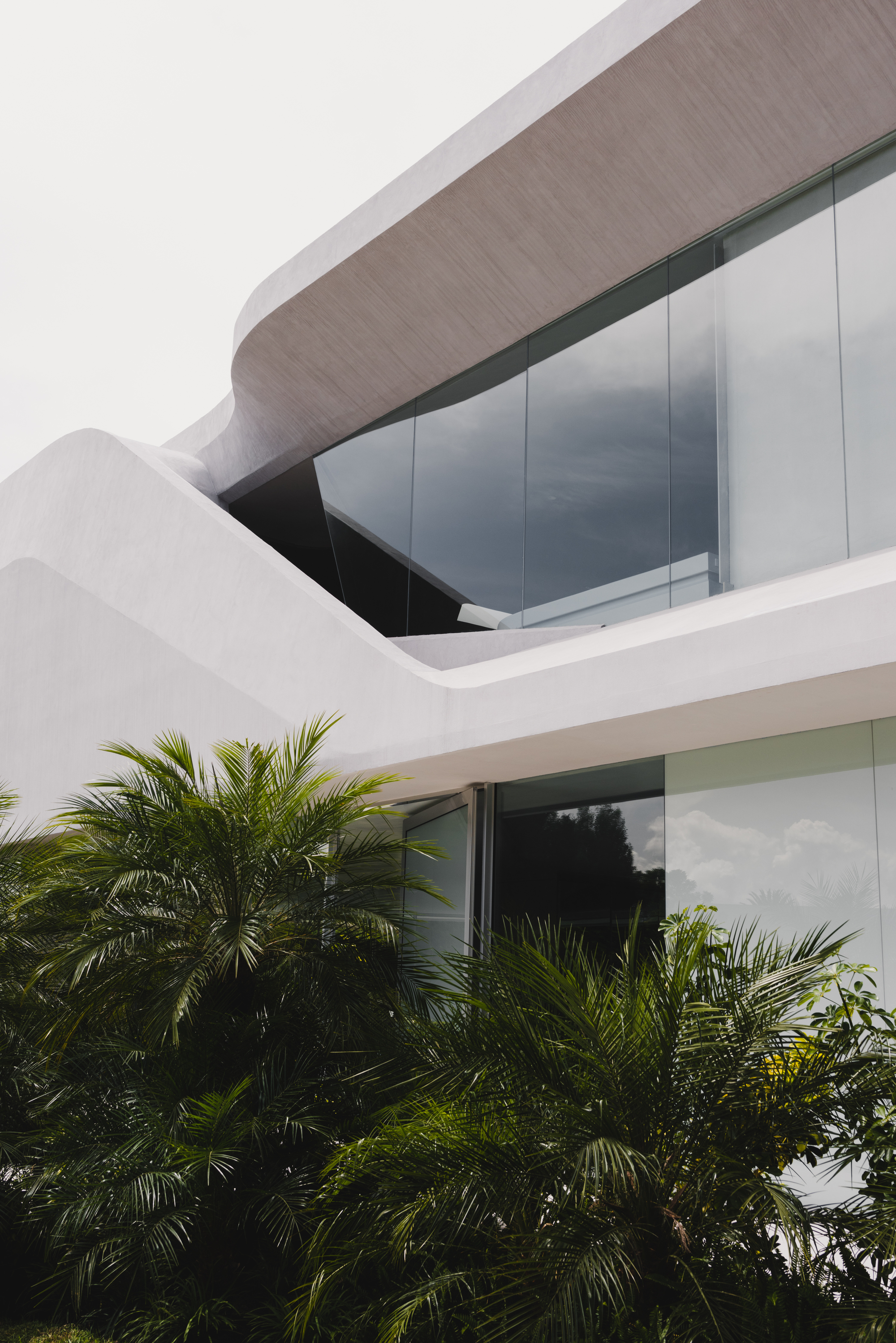 Exterior facade detail showing the curved upper balcony soffit with palms in the foreground