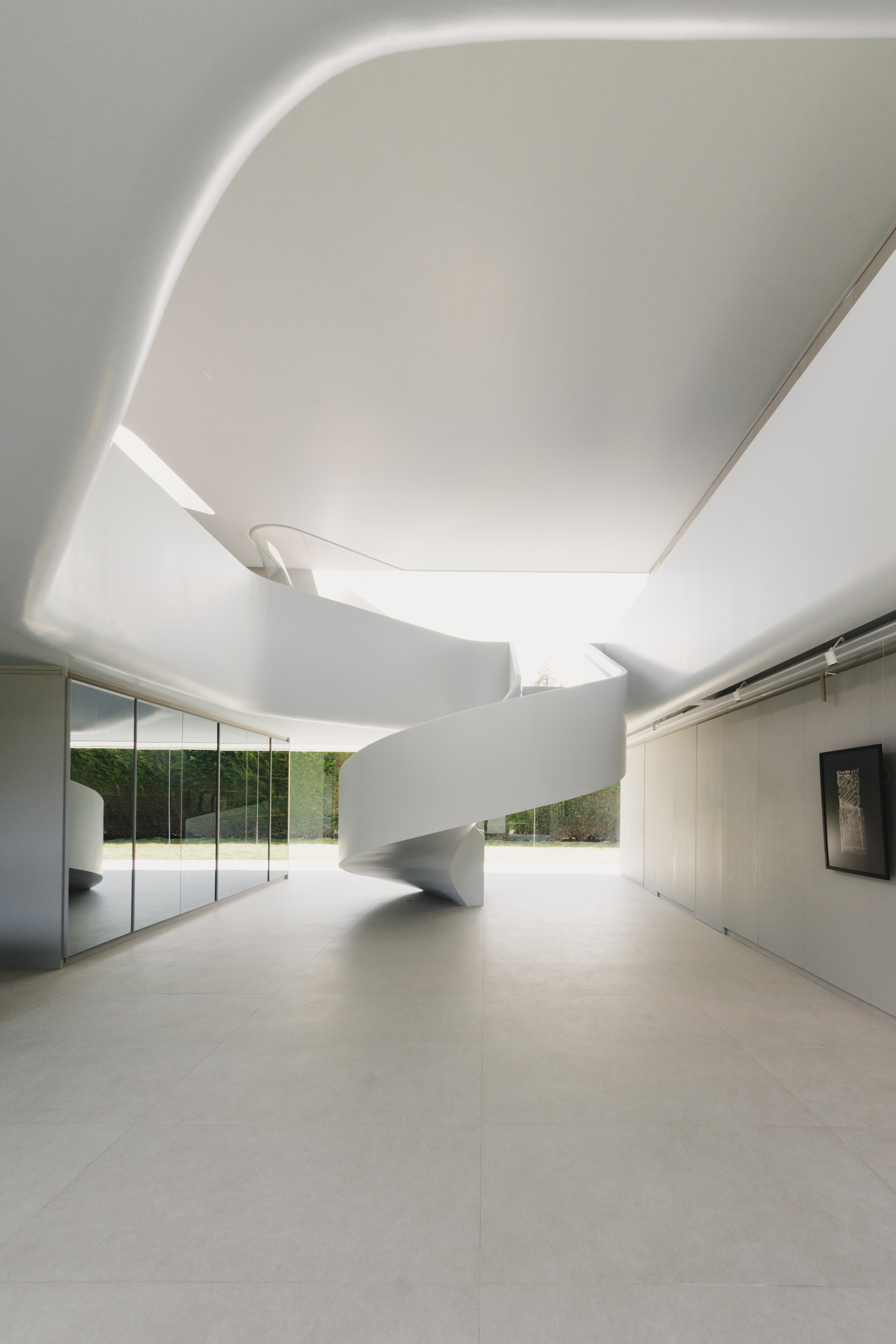 Curved white spiral staircase beneath a sculpted ceiling with concealed perimeter lighting