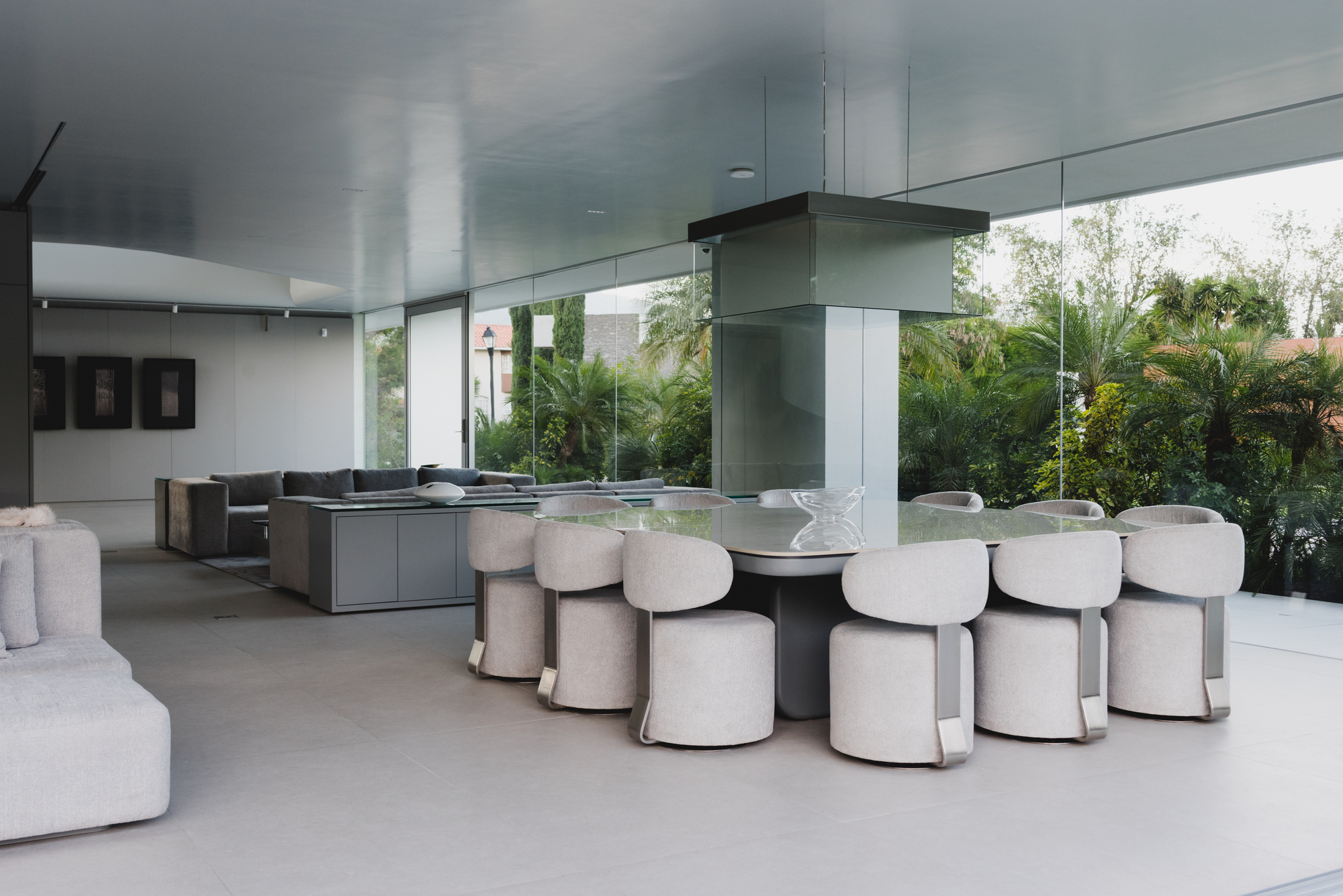 Open-plan living area with upholstered seating around a central kitchen island overlooking garden palms