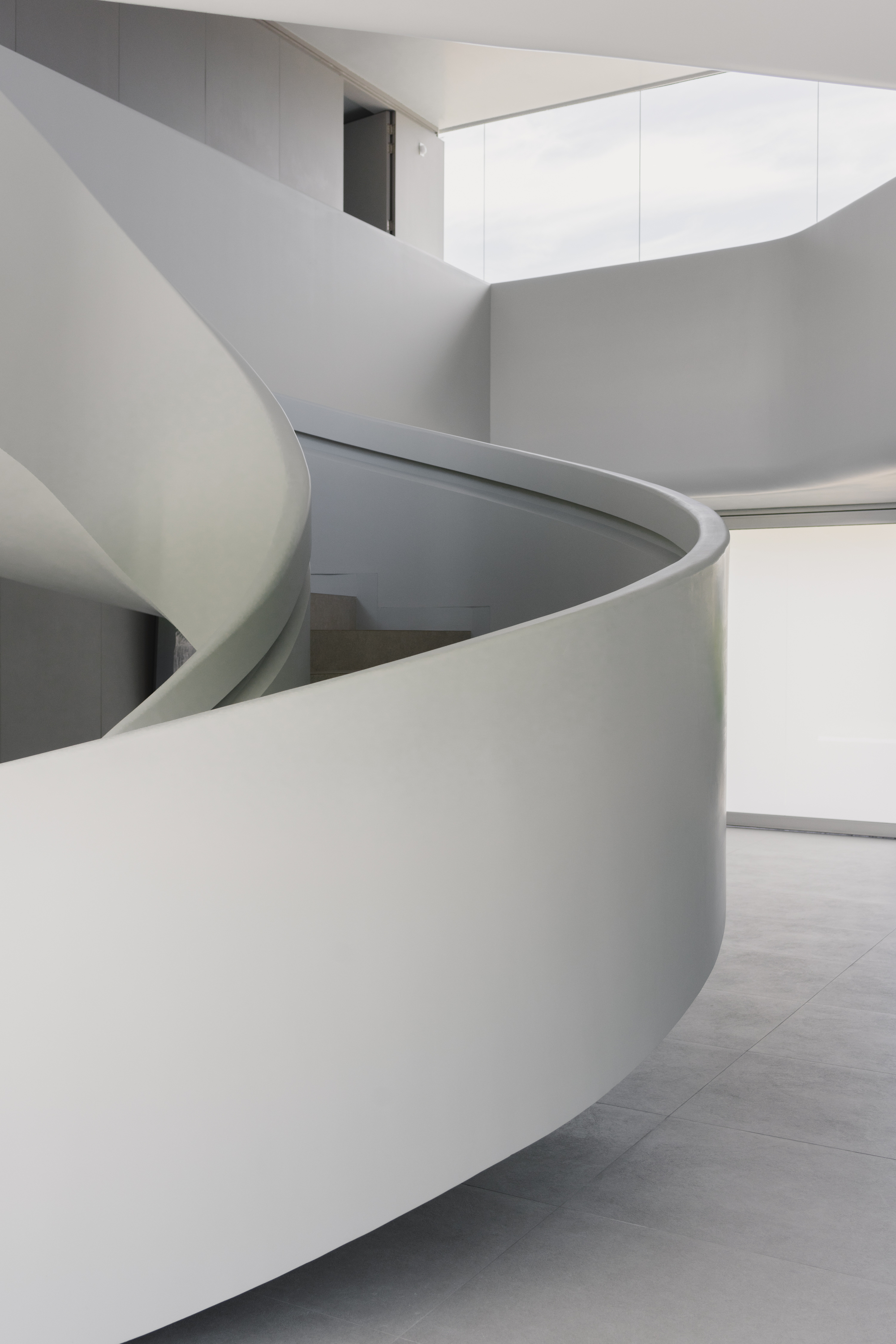 Spiraling white staircase with smooth curved walls rising through a light-filled interior space