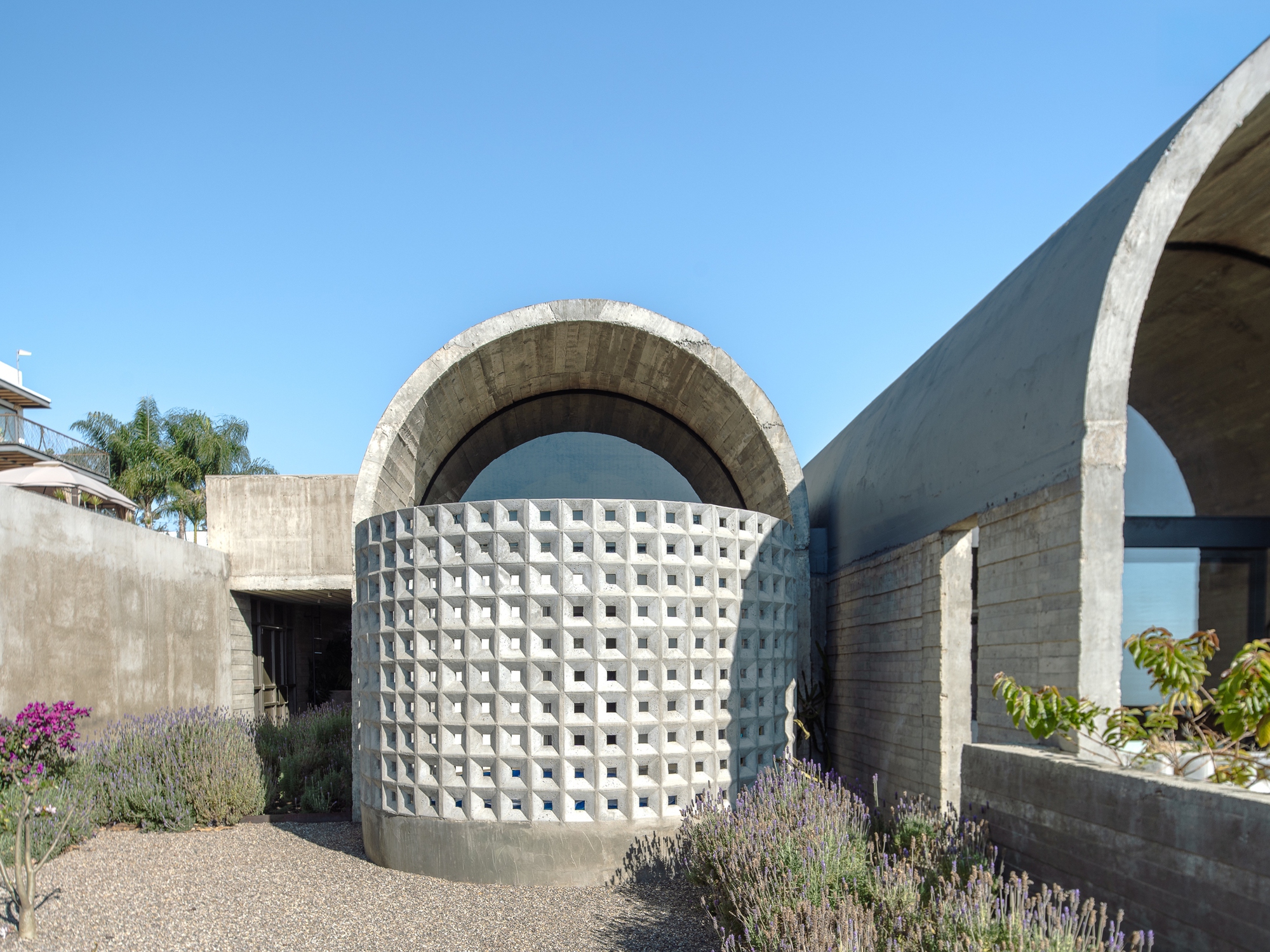 Perforated concrete screen wall beneath a barrel vault with lavender and flowering plants in foreground