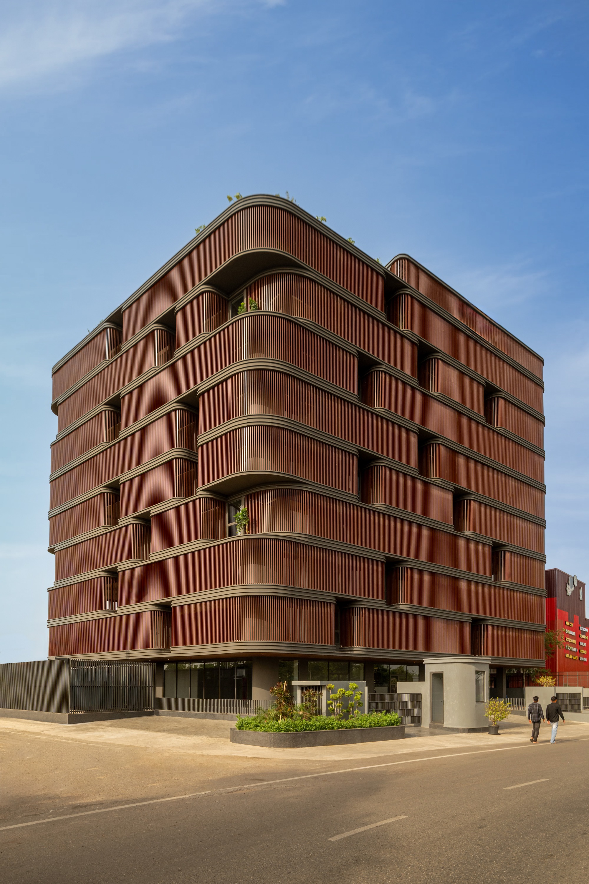 Corner view of the building with curved terracotta slat balconies and rooftop greenery under clear sky