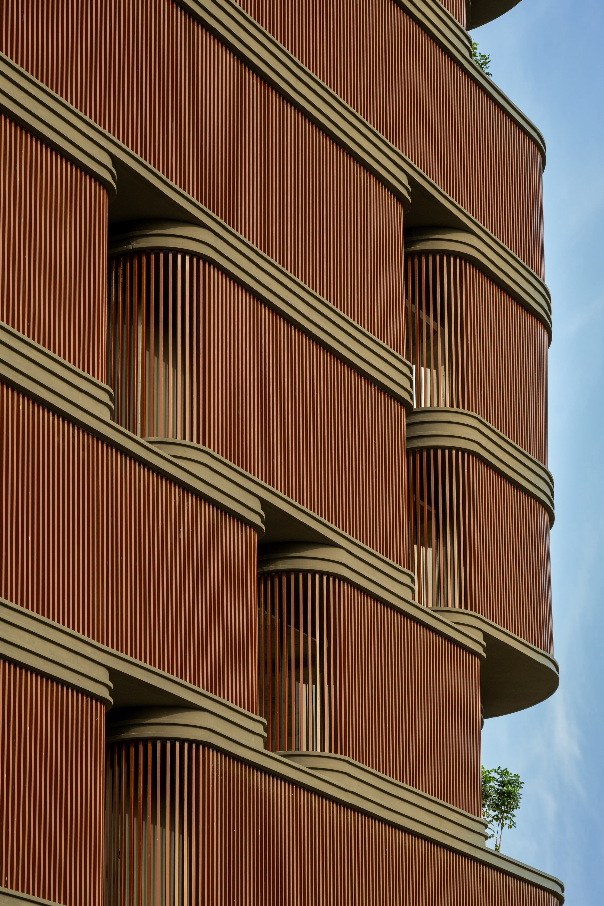 Close-up of the curved facade showing vertical terracotta louvers and recessed balconies with metal trim