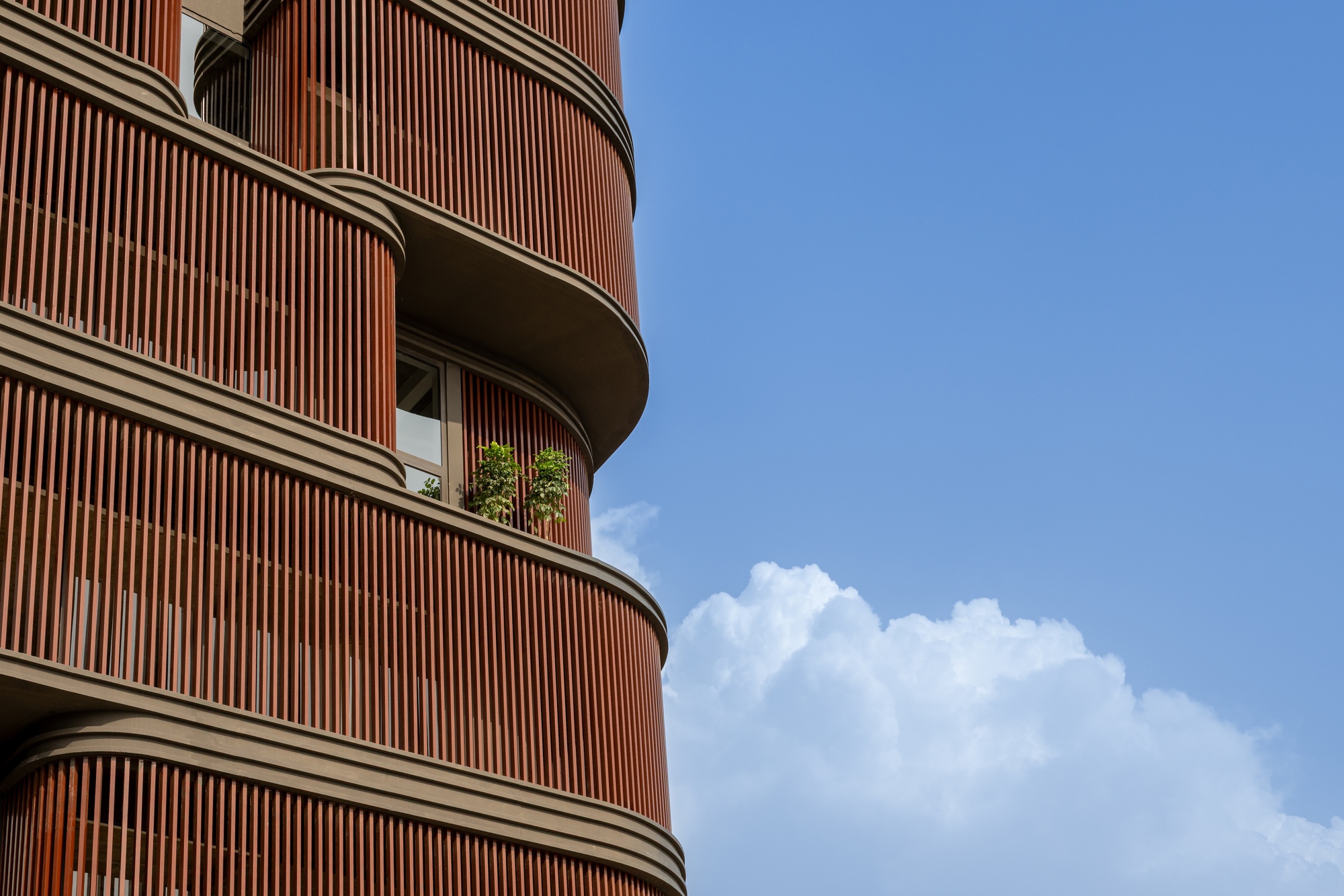 Curved timber facade with recessed balconies beneath white cumulus clouds
