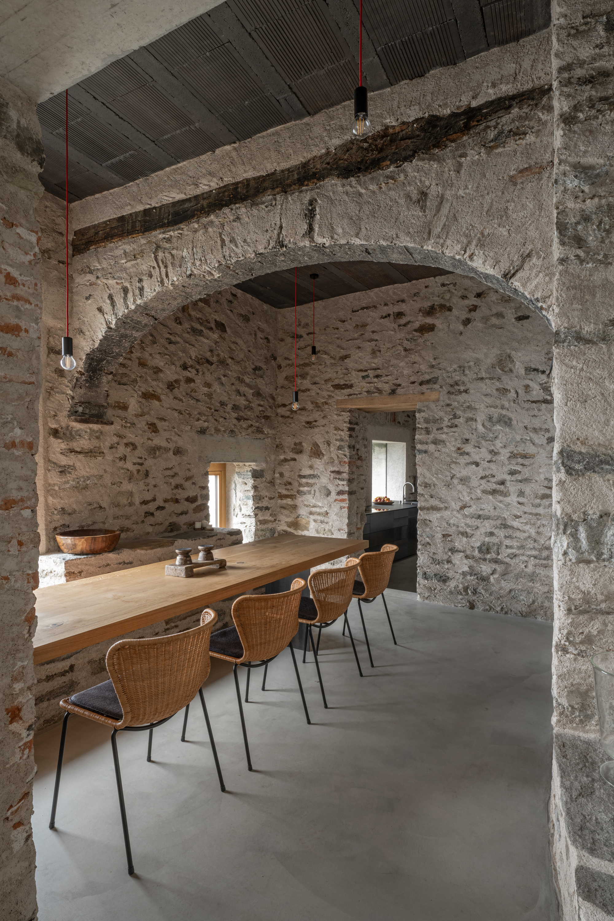 Dining room with exposed stone masonry arch and long timber table beneath a corrugated metal ceiling