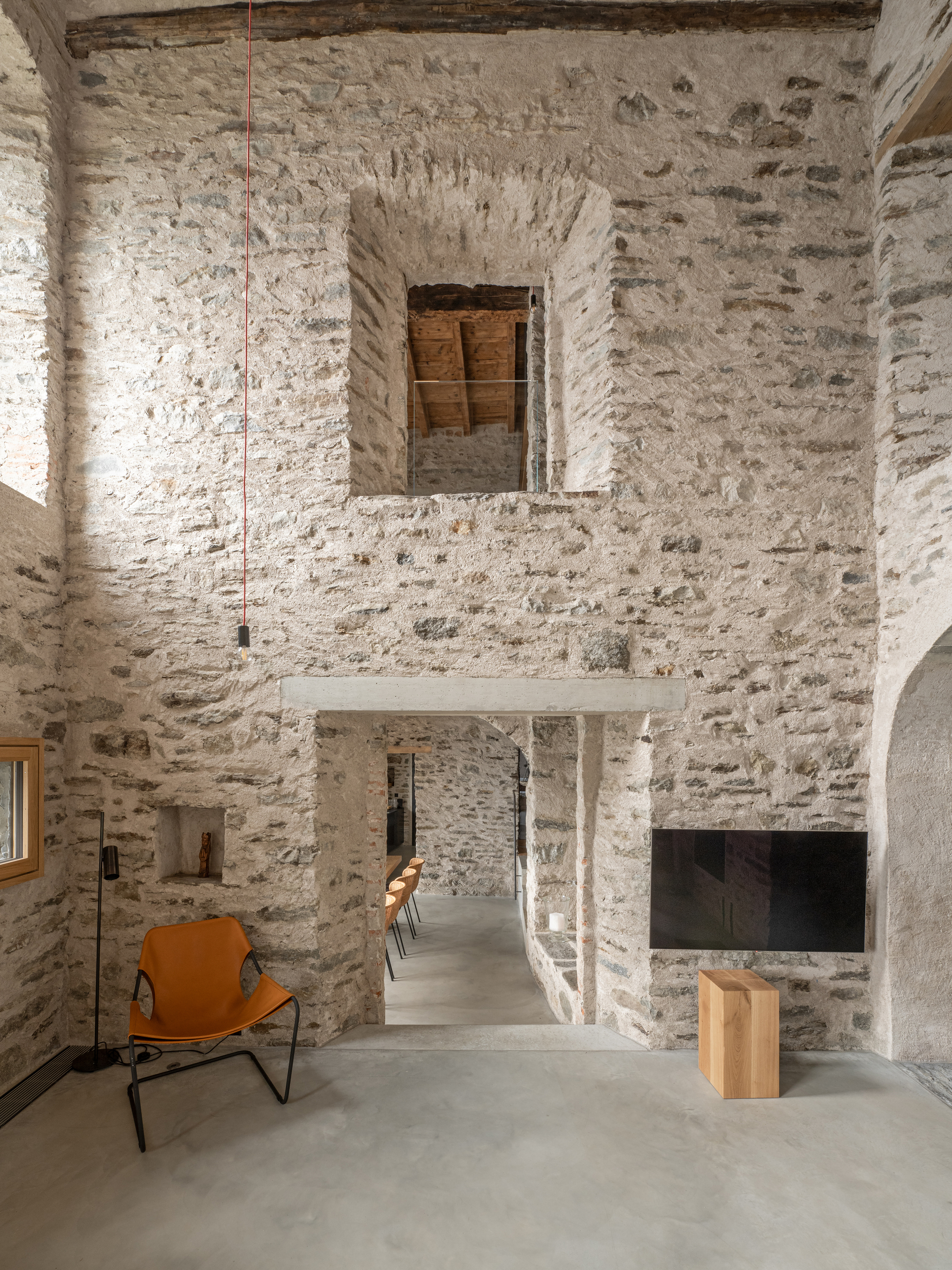 Double-height interior space with whitewashed stone walls and suspended mezzanine slab beneath pendant lights