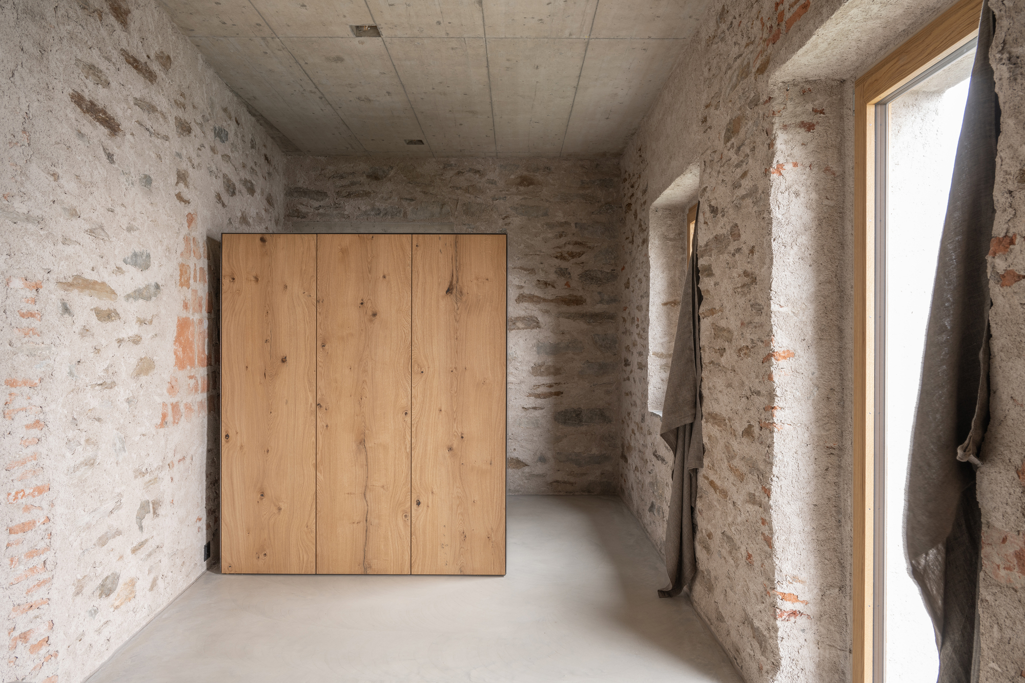 Interior corridor with exposed stone masonry walls, timber wardrobe, and polished concrete floor