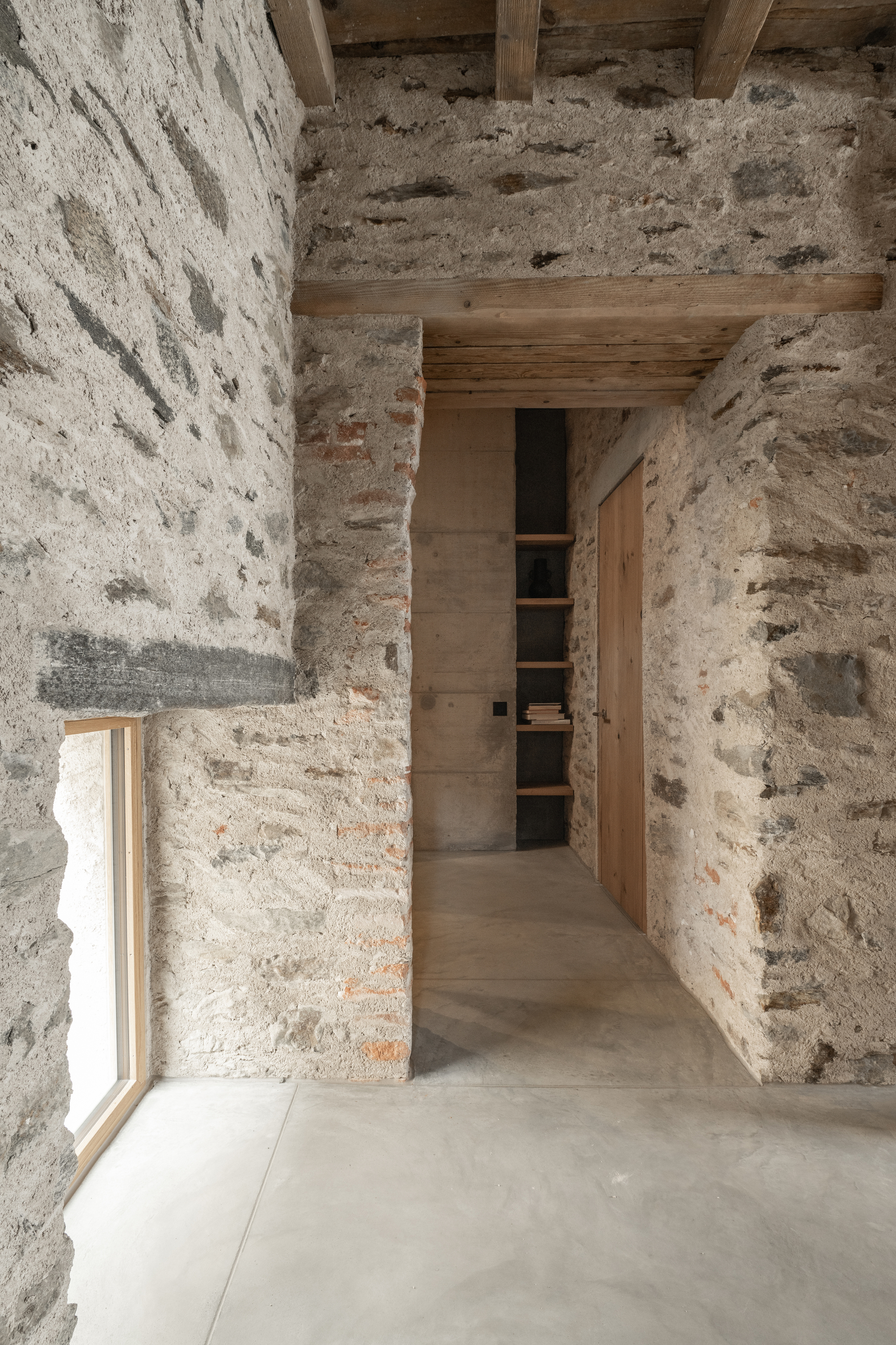 Corridor view between exposed stone walls with timber beams above and polished concrete floor