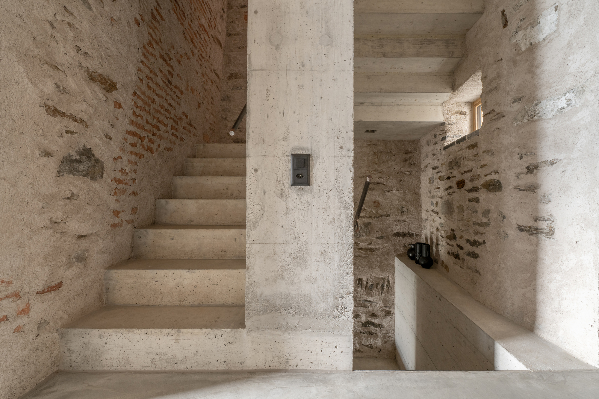 Concrete staircase ascending alongside a structural column within stone and brick walls