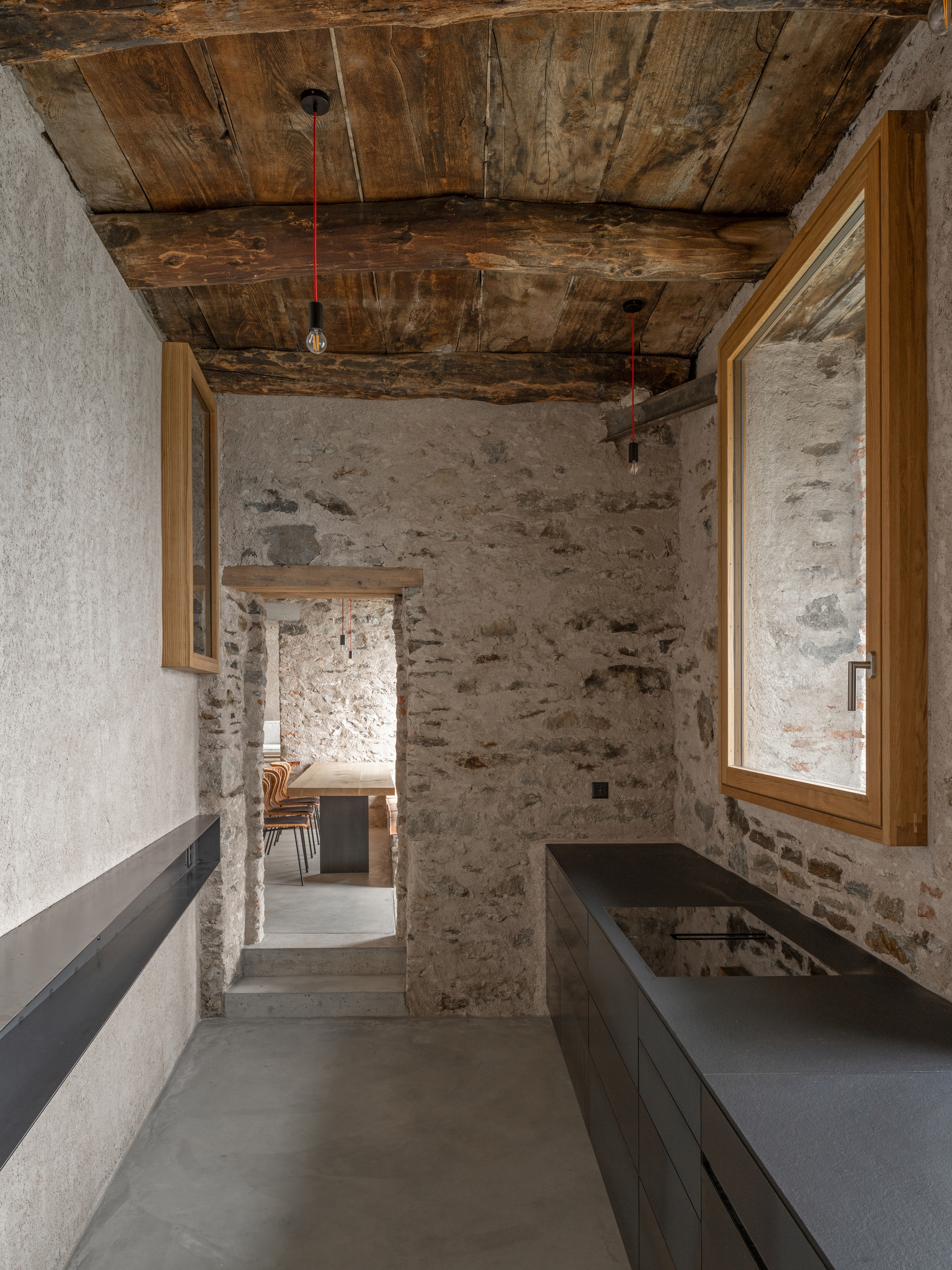 Interior passage with dark cabinetry along rough stone walls under timber plank ceiling with pendant lights