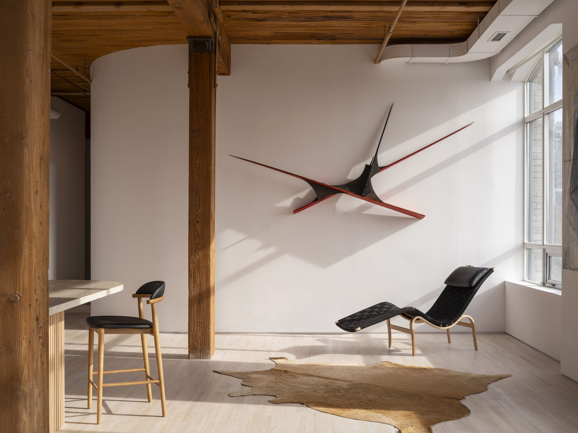 White wall with sculptural black and red artwork above a chaise lounge near sunlit windows