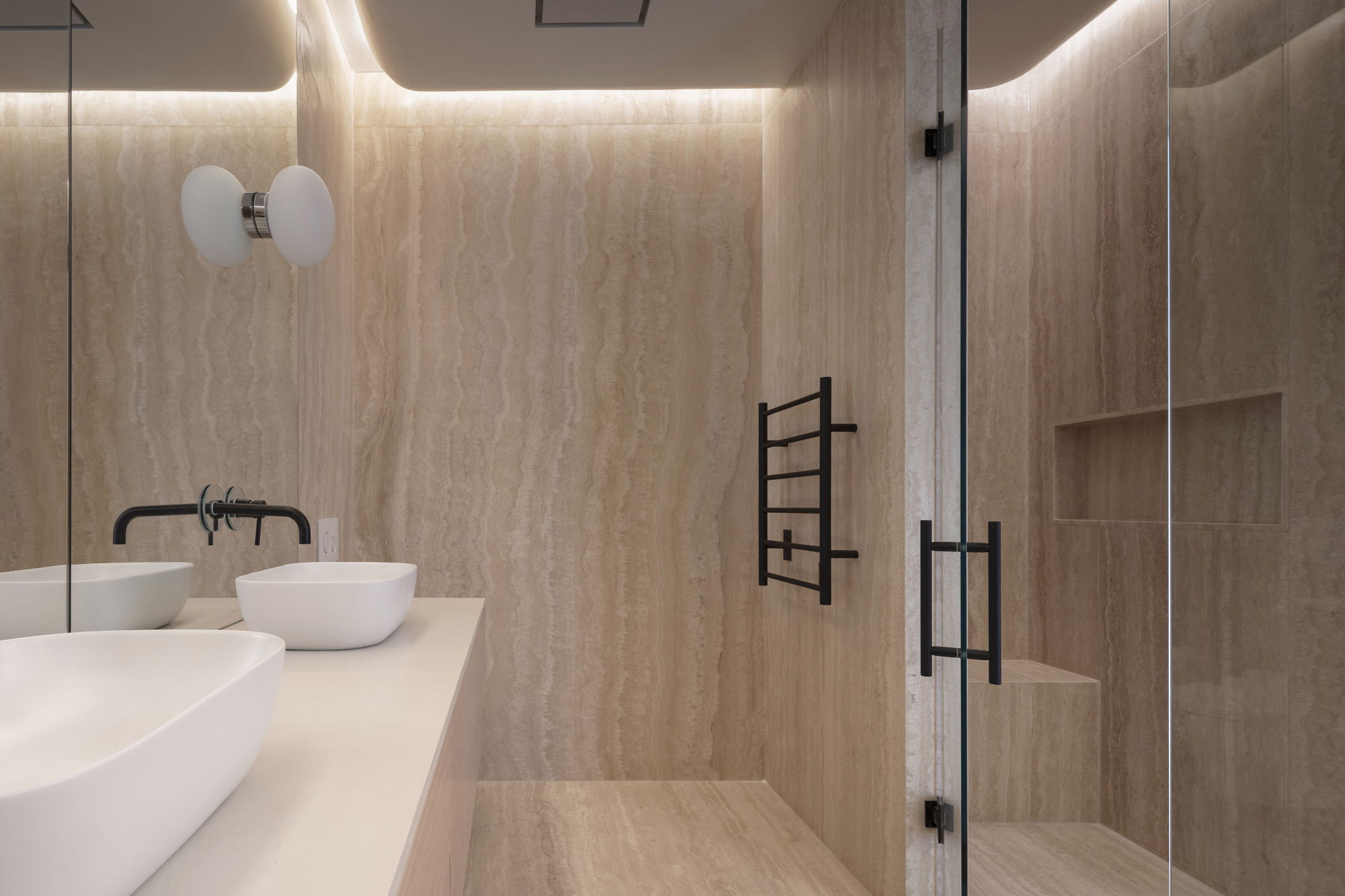 Bathroom with travertine walls, cove lighting, glass shower enclosure and floating double vanity