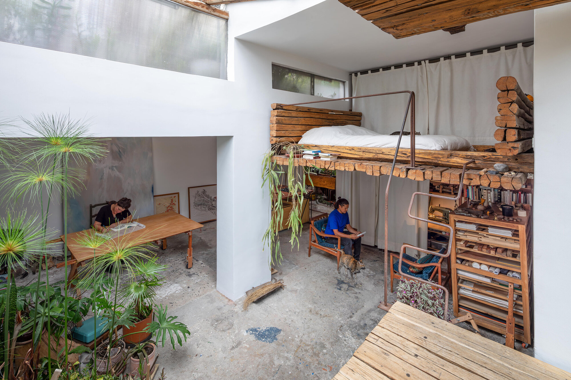 Interior courtyard with suspended timber loft bed and open-air workspace surrounded by potted plants