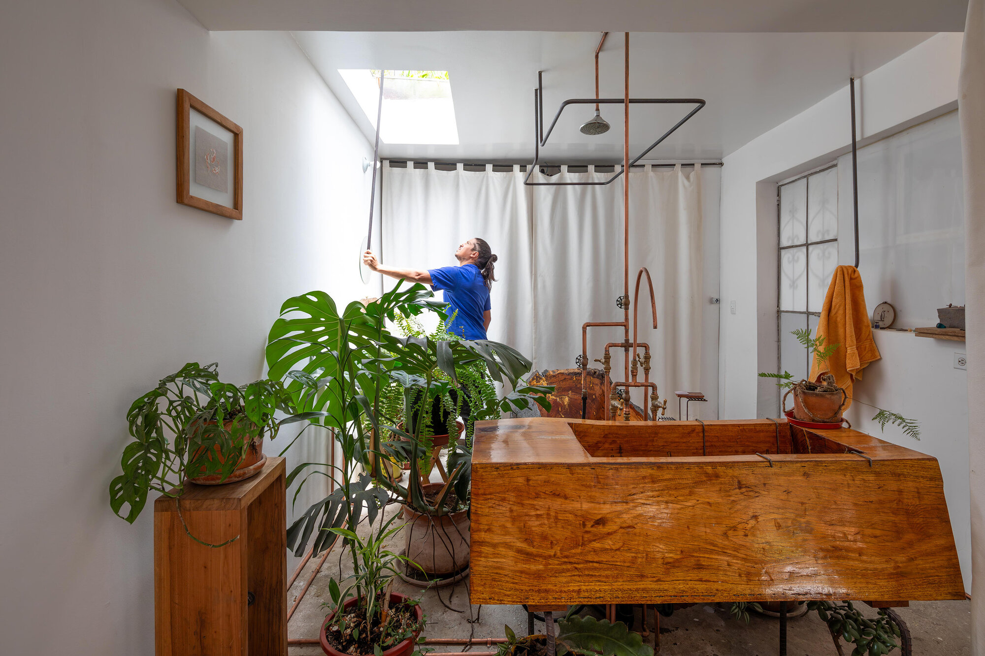 Bathroom with live-edge timber vanity, exposed copper plumbing, and skylight above white curtain