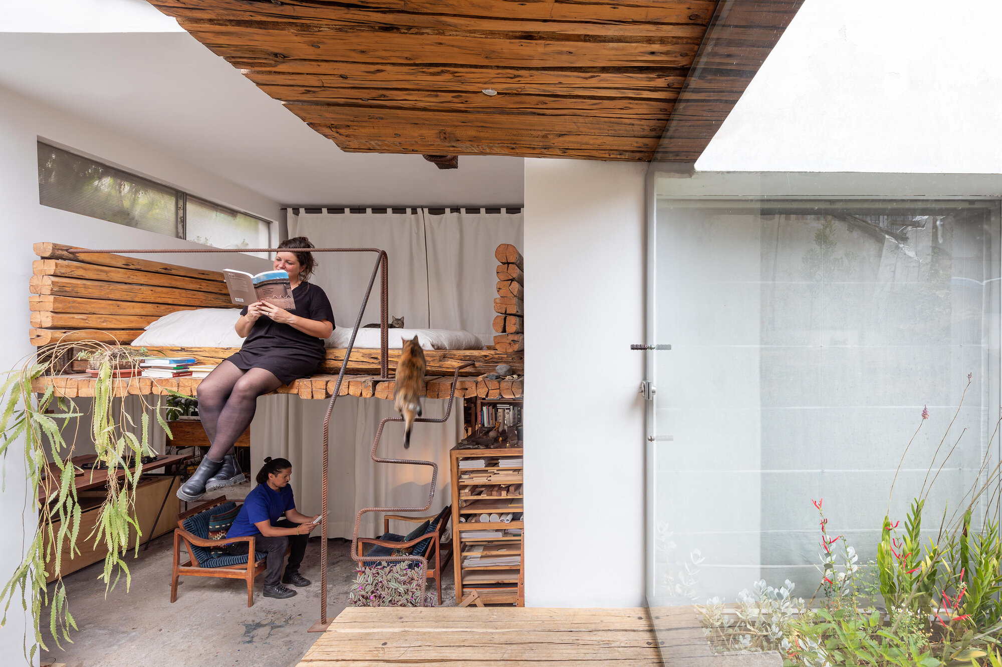 Timber sleeping loft with slatted platform suspended above a workspace with two people