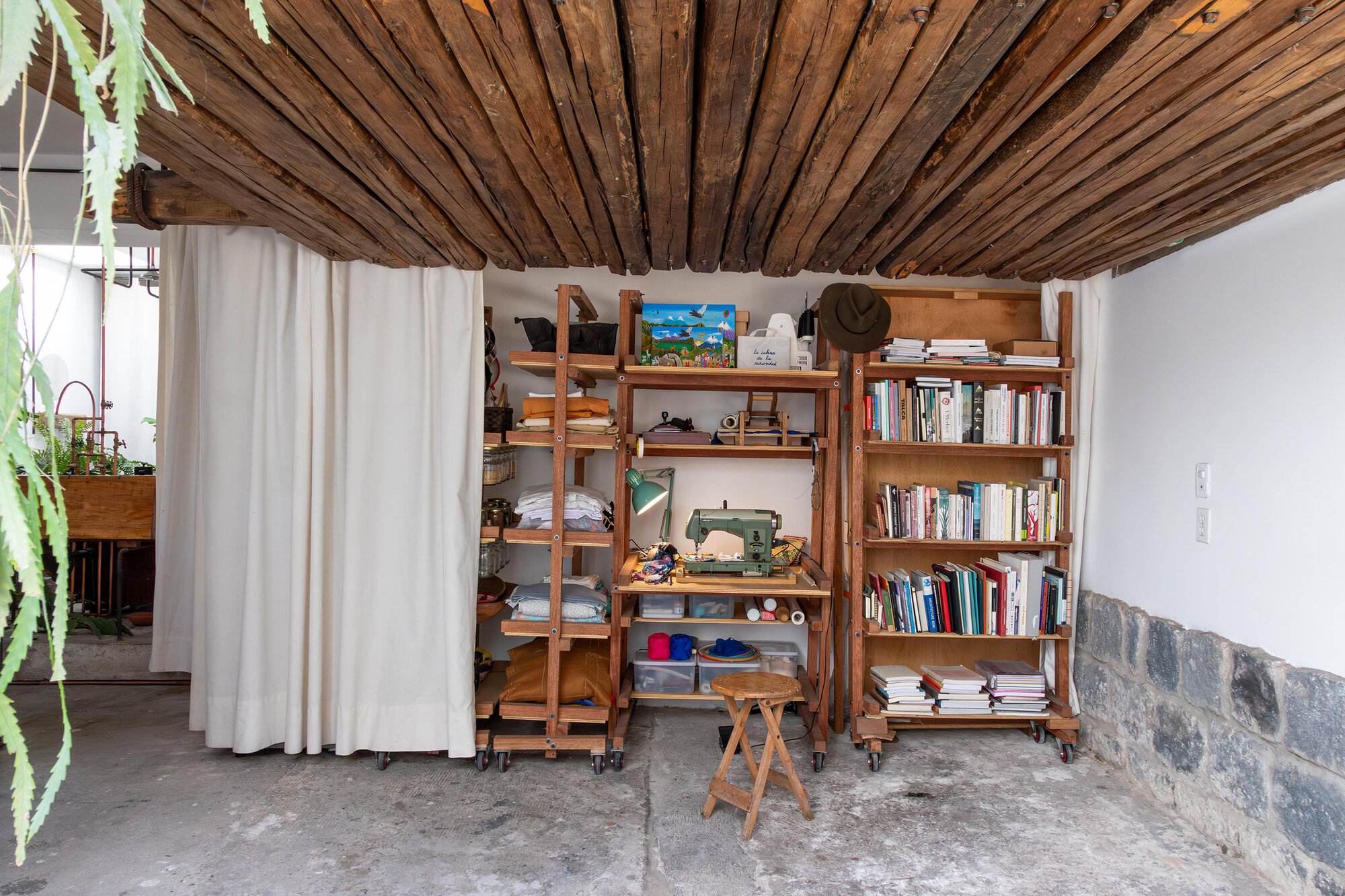 Reclaimed timber plank ceiling above wheeled storage units and a fabric curtain divider