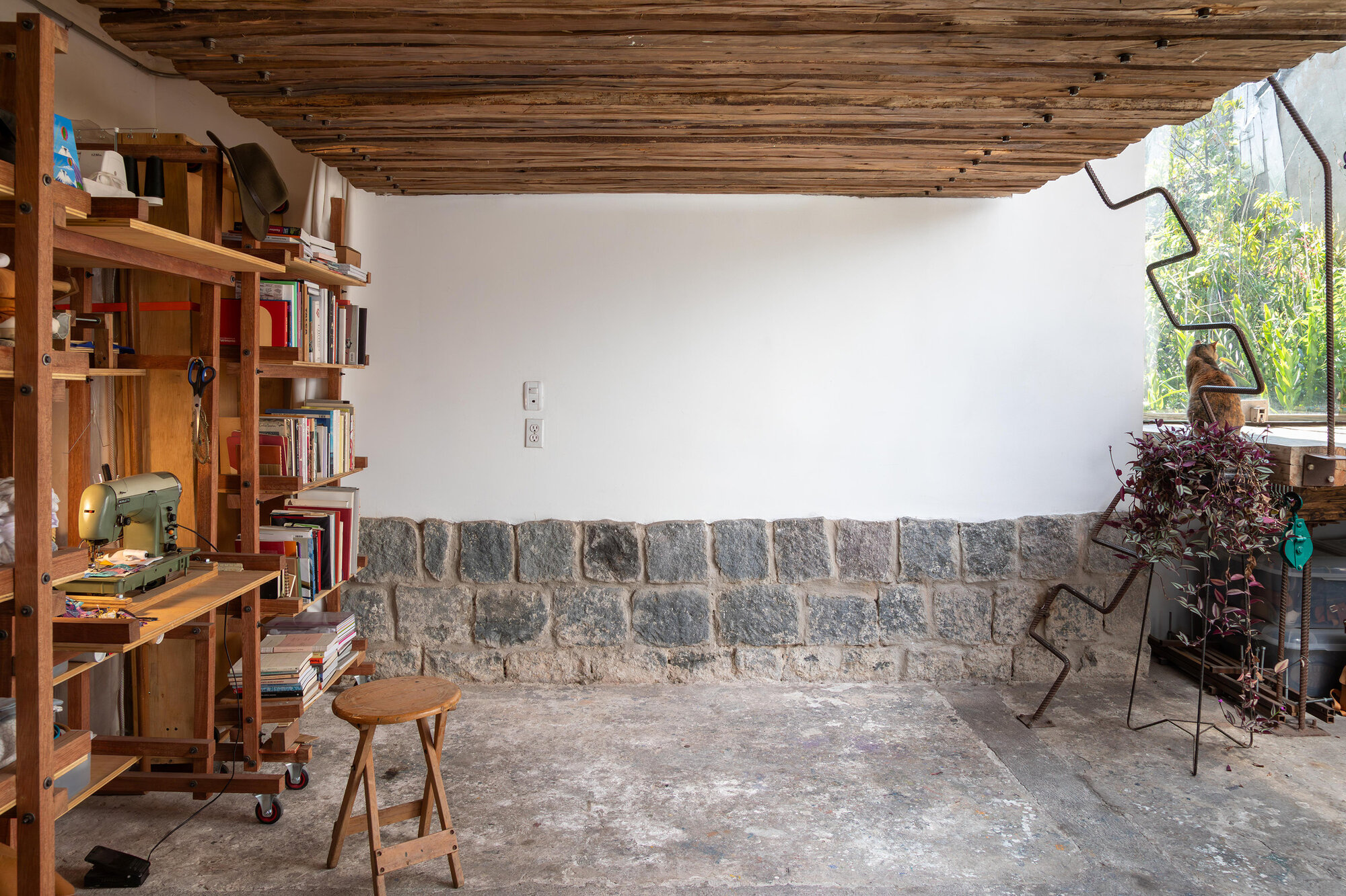 Exposed stone masonry base wall with timber shelving and a sewing machine on wheeled cart