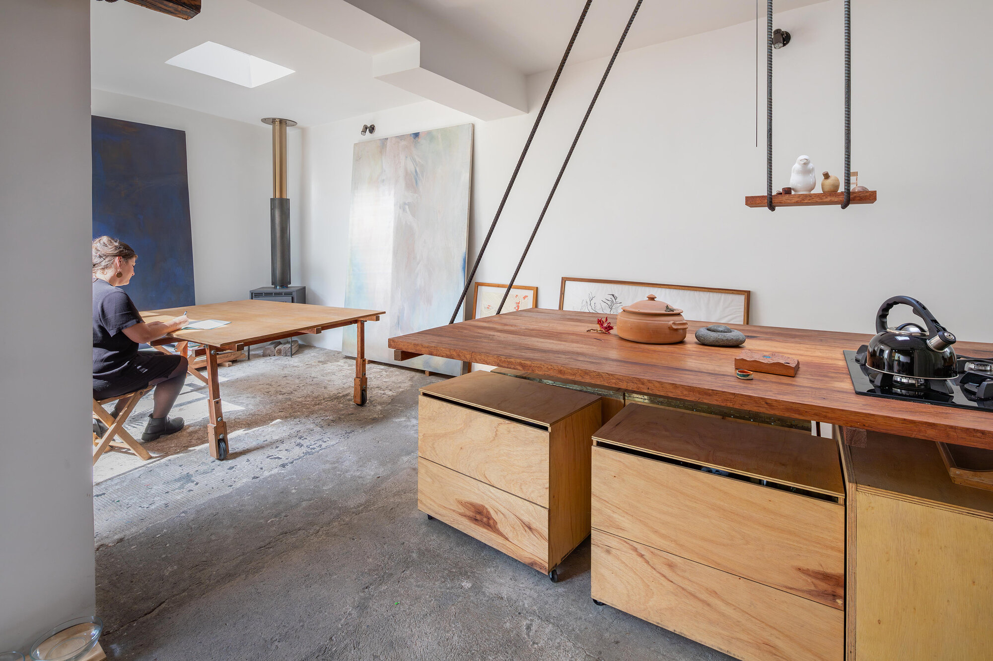 Interior with collapsible timber dining table and modular kitchen counter on concrete slab floor