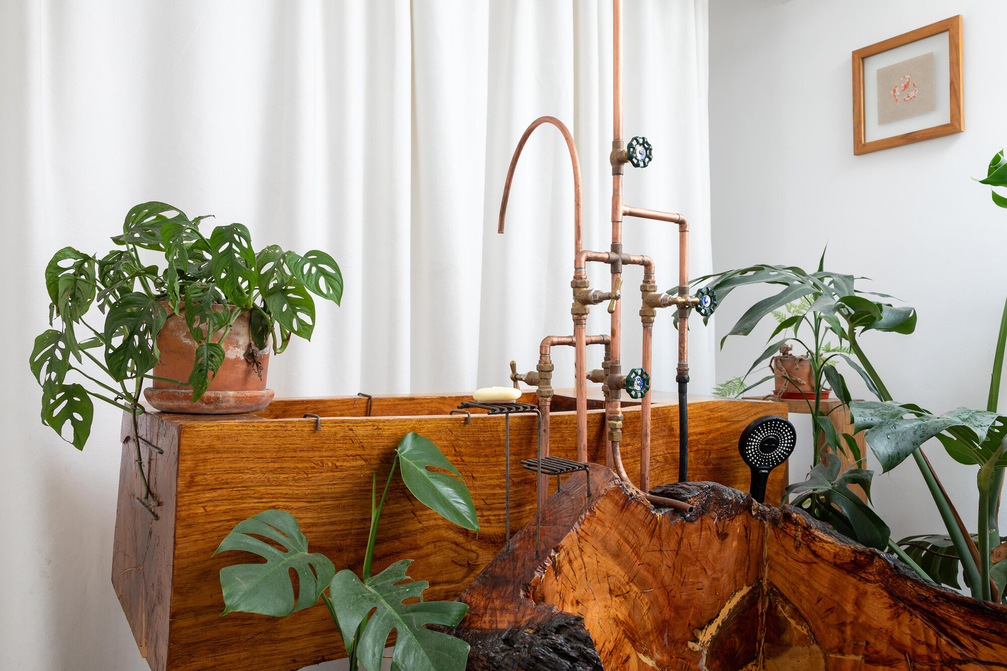 Custom copper pipe faucet rising from timber bathtub with houseplants on the rim
