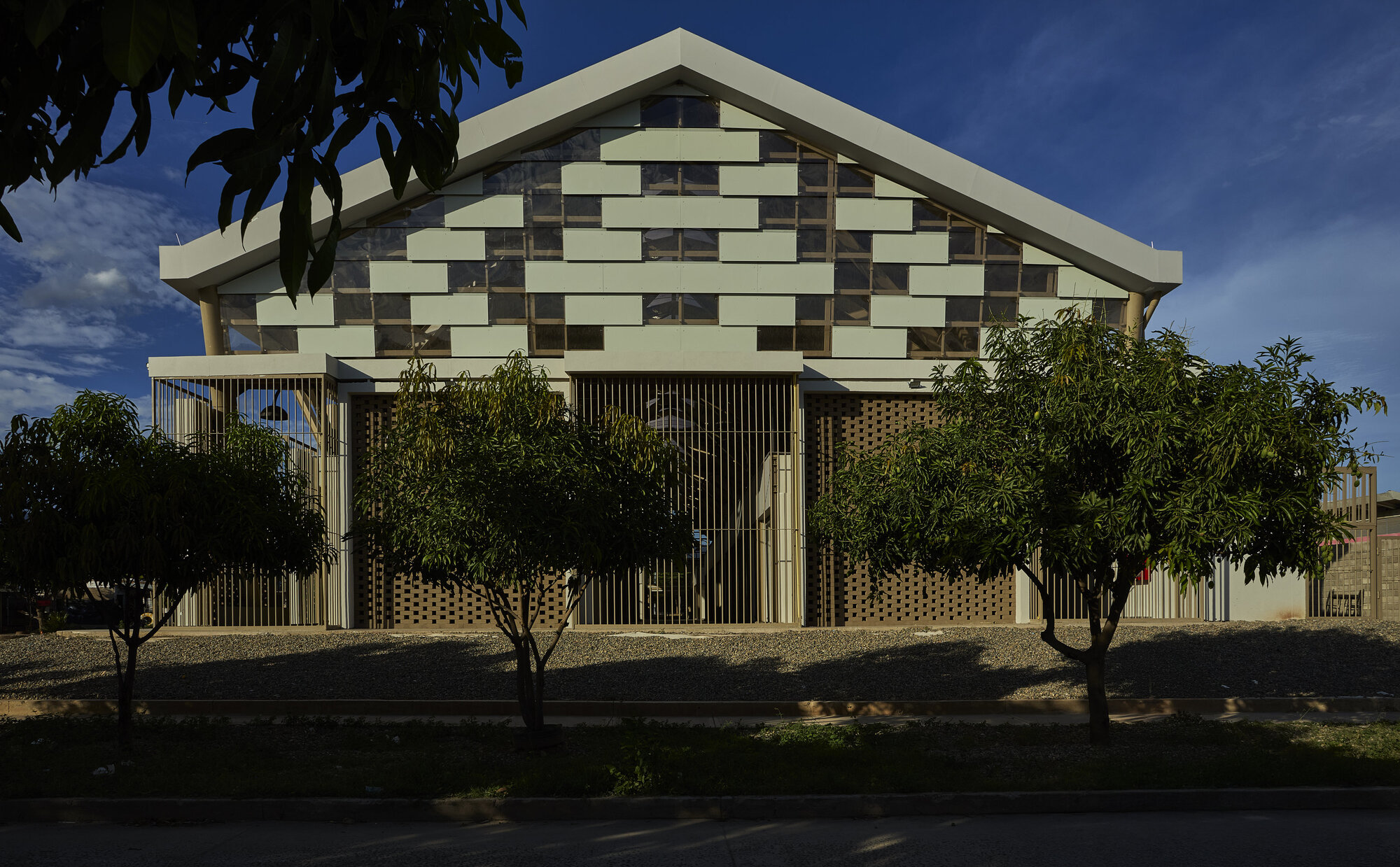 Gabled facade with chequered panel pattern above a perforated brick ground floor screened by young trees