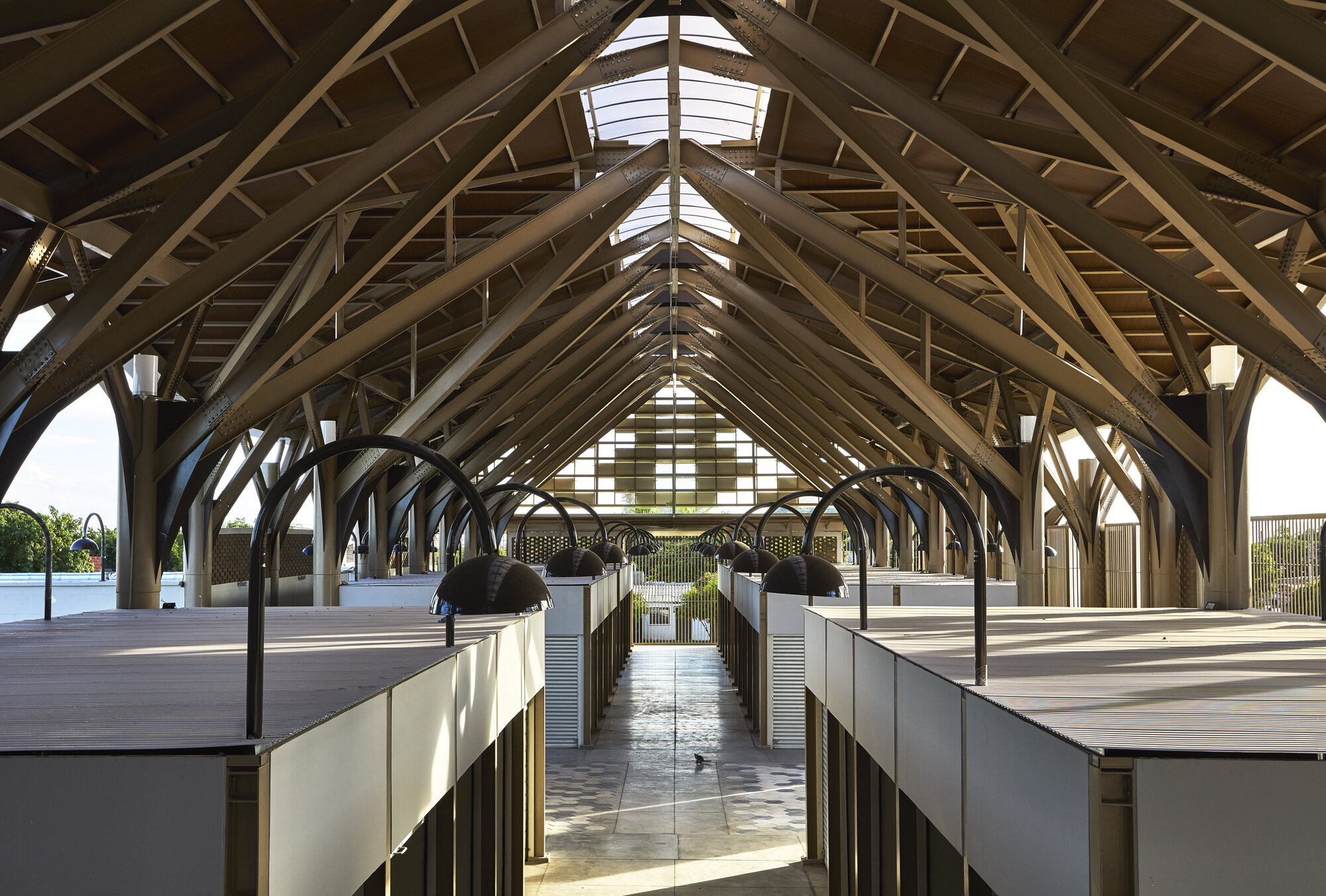 Central corridor under timber truss roof with skylights and a person walking toward the gabled end