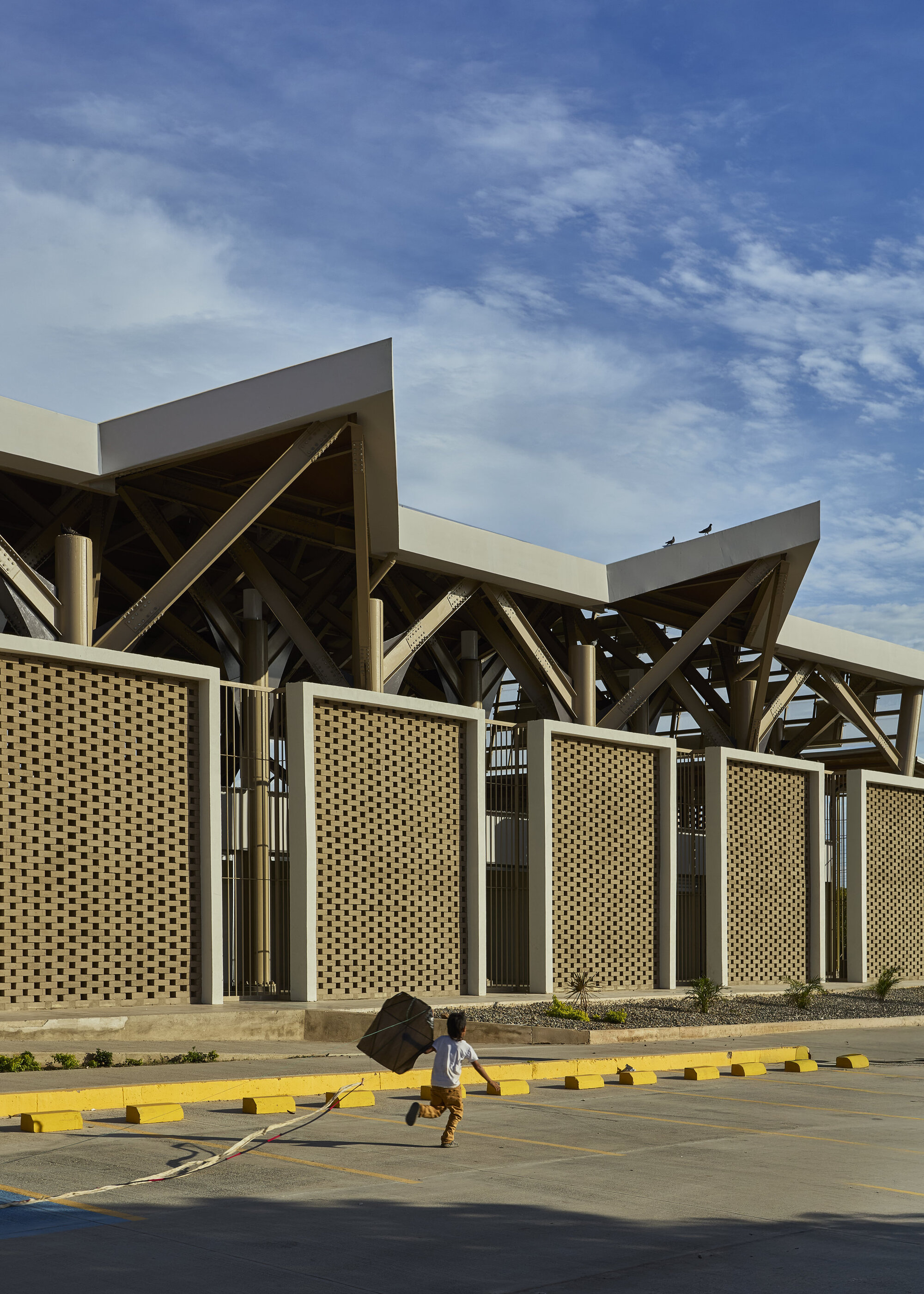 Exterior perimeter showing lattice screen wall and exposed timber roof structure as a person crosses the parking lot