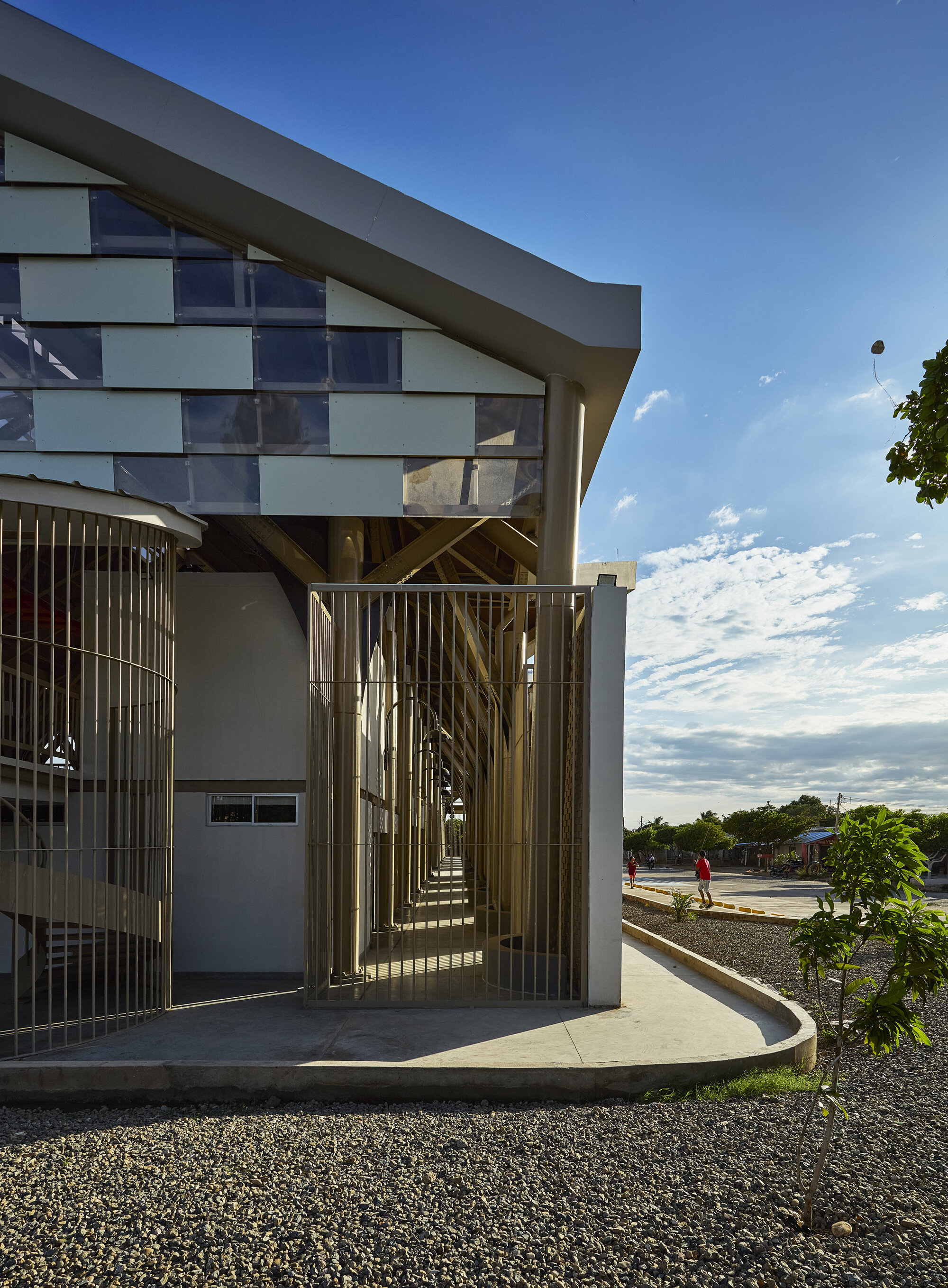 Entrance with vertical metal screen and curved concrete platform under a cloudy afternoon sky