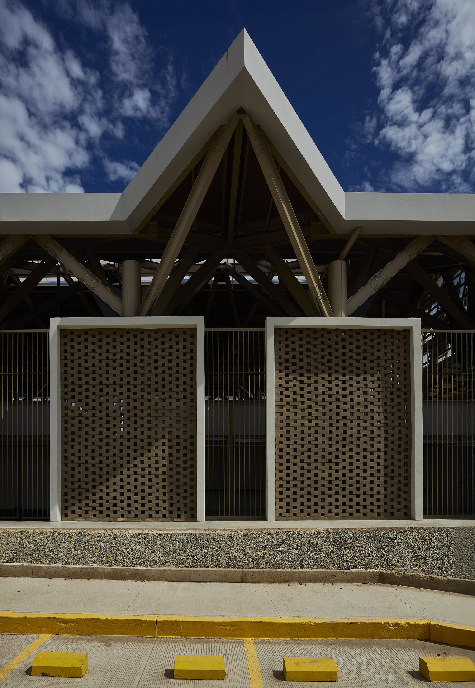 Perforated timber screen panels framed in white beneath an angular gabled roof under blue sky