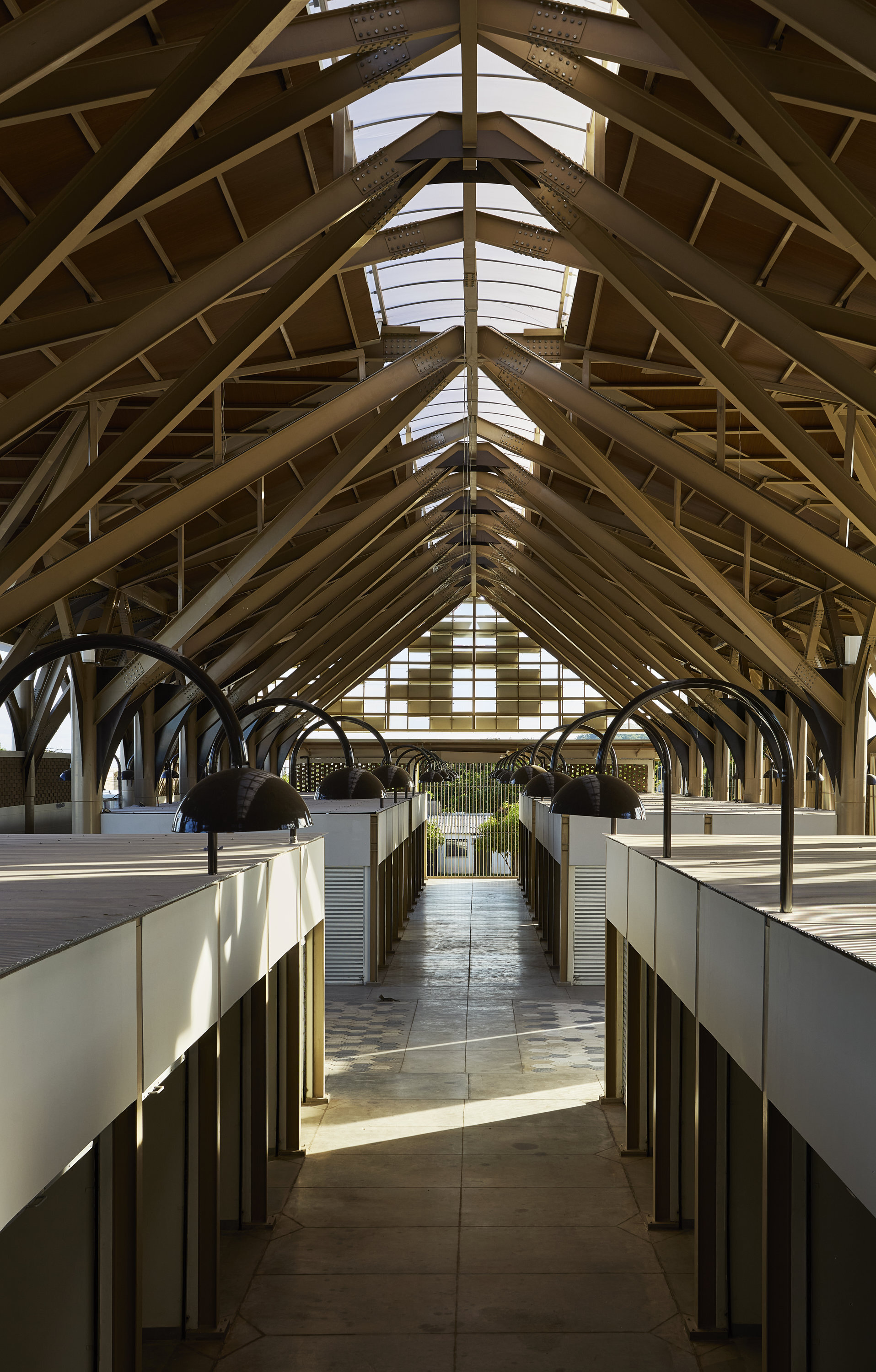 Central aisle with timber arched ceiling, skylights, arched pendant lamps, and flanking vendor stalls