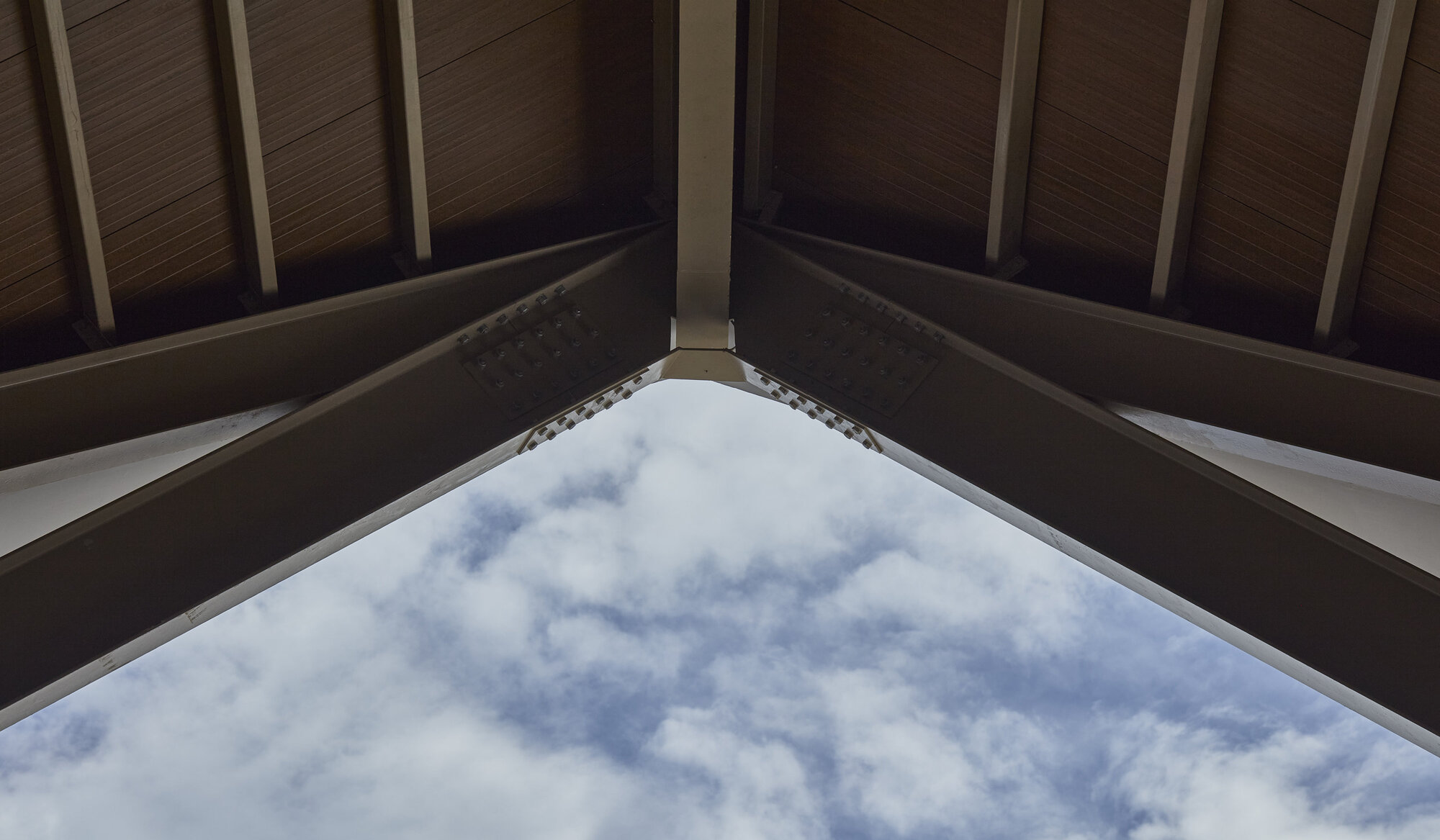 Upward view of the peaked skylight framed by timber rafters against scattered clouds