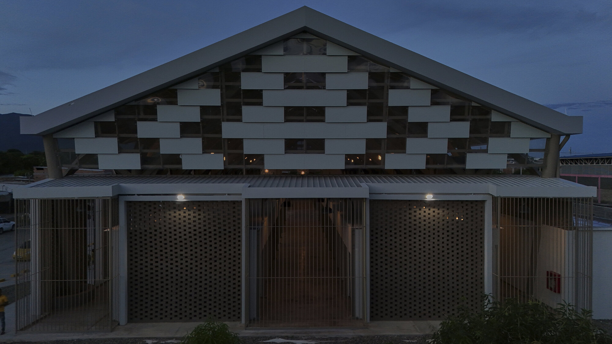 Gabled facade with chequered panel pattern above perforated timber screens at twilight
