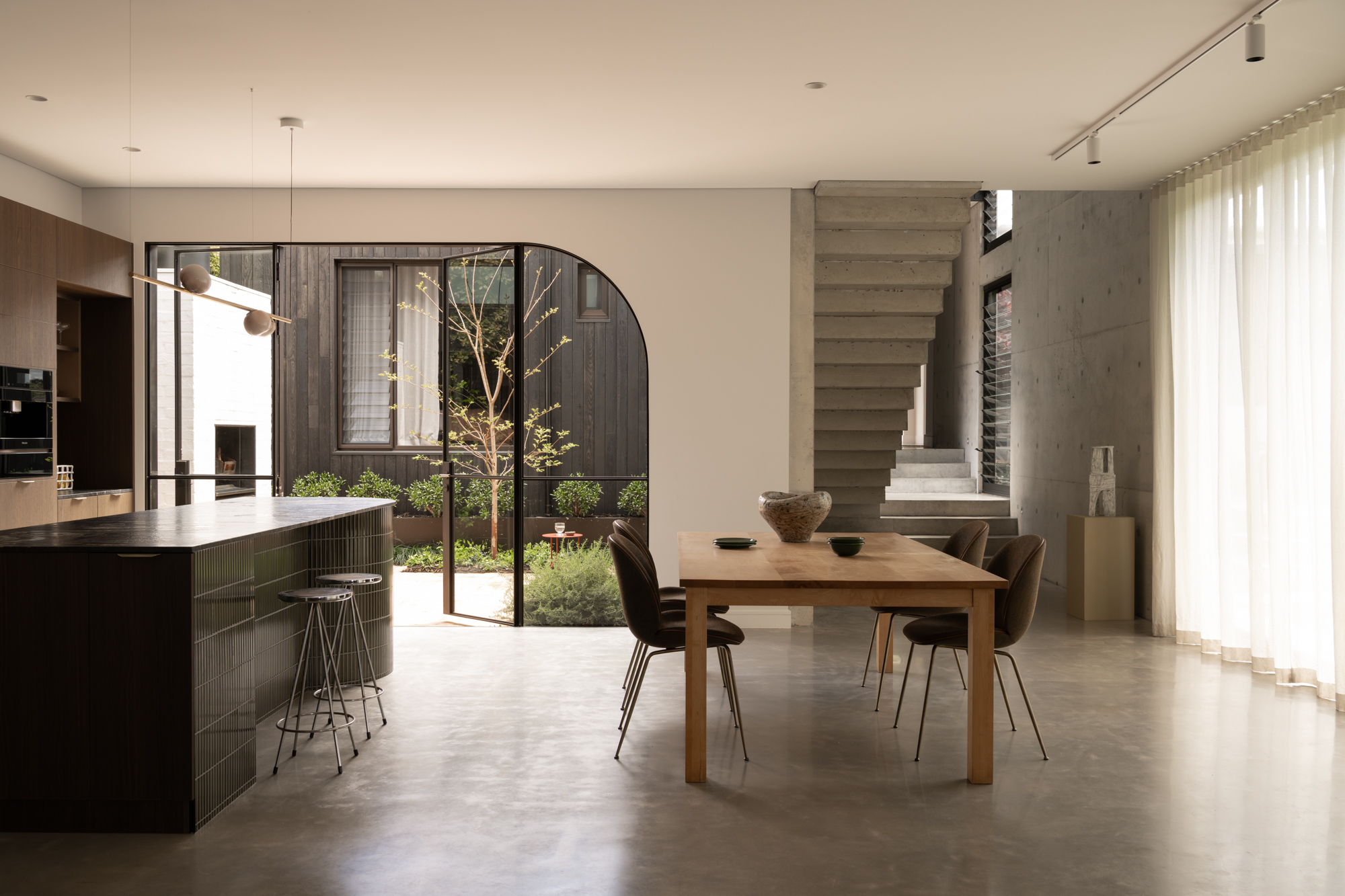 Open-plan dining area with arched glass doors to courtyard, concrete staircase, and polished concrete floor