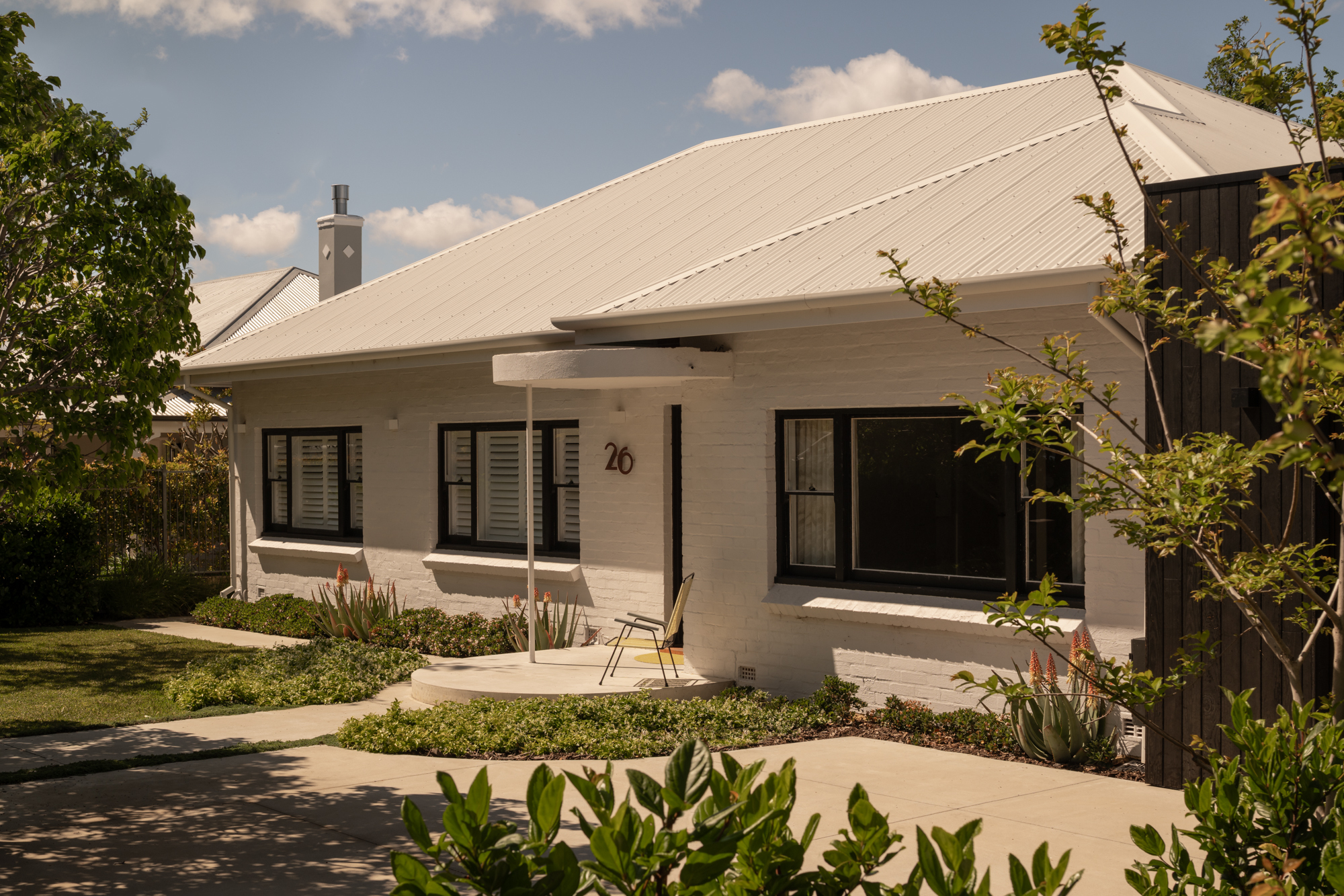 Front facade with corrugated metal roof and planted garden beds under afternoon light