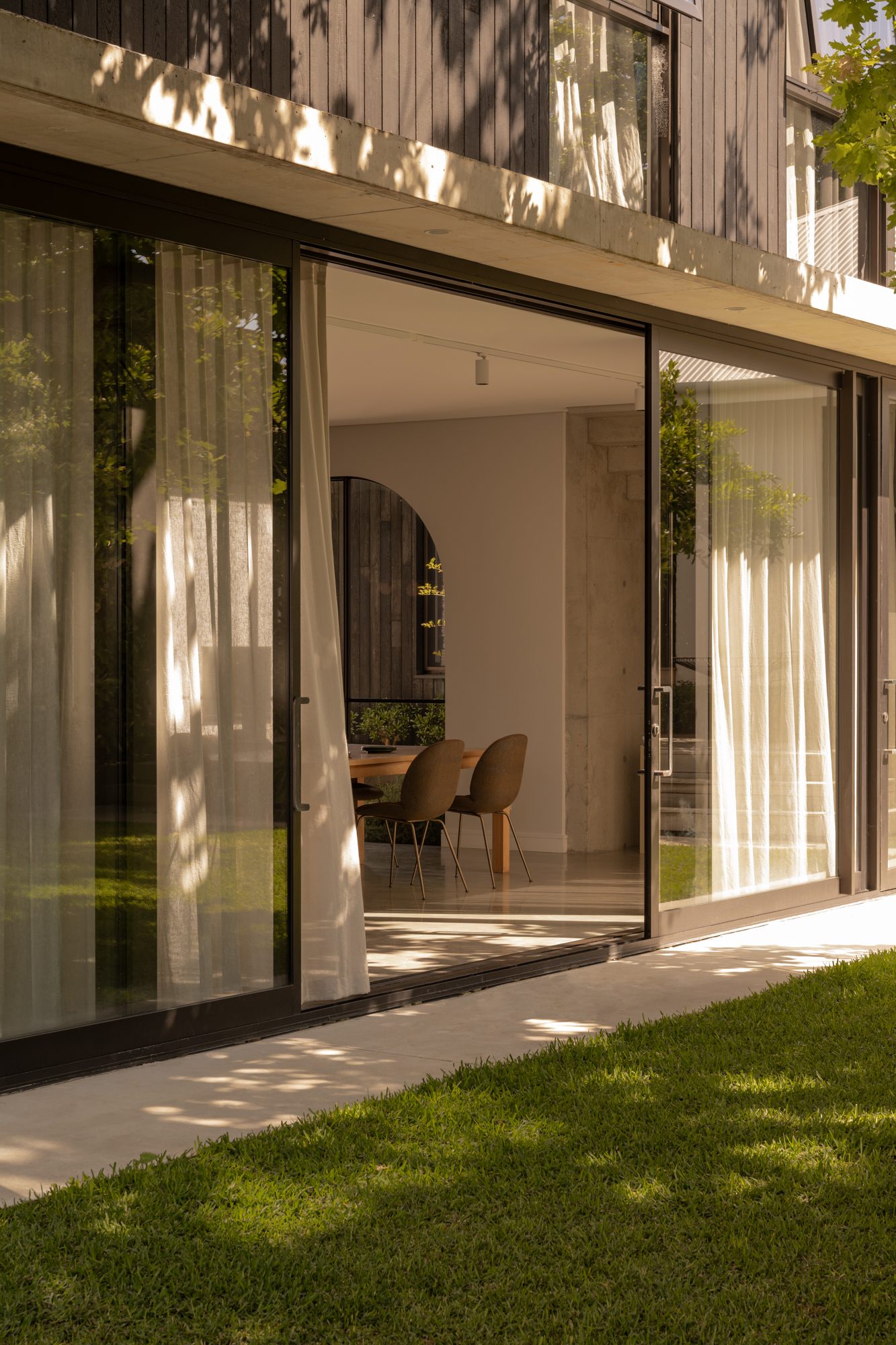 Glass sliding doors opening from lawn to dining room with timber-clad upper level