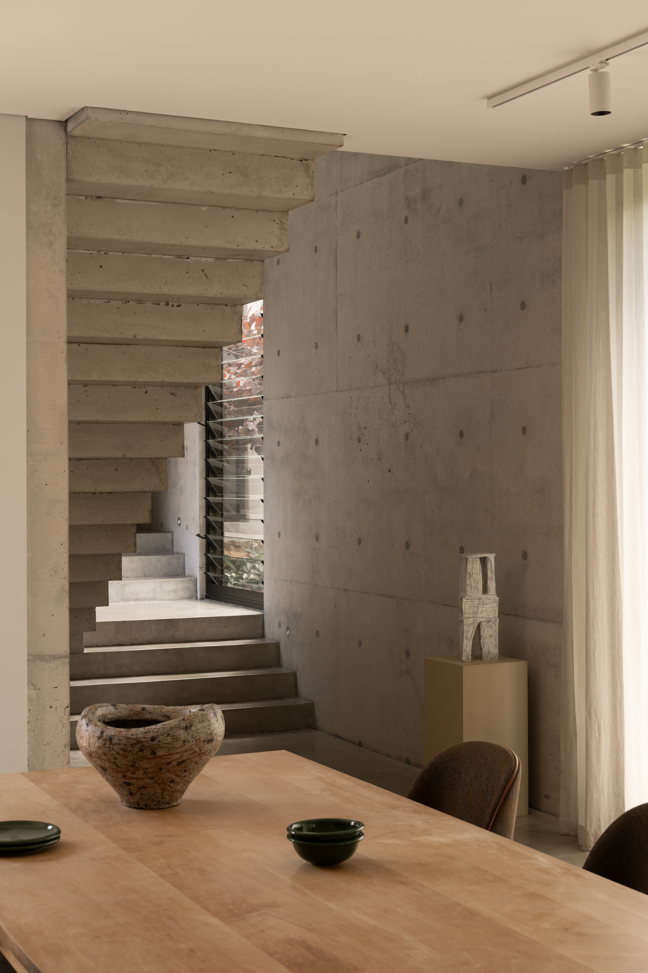 Board-formed concrete staircase rising between walls with a vertical slot window above