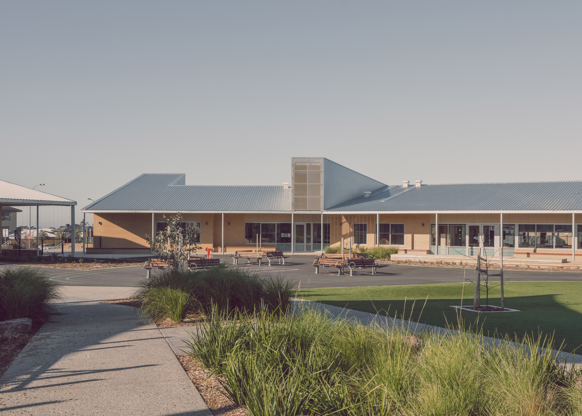 View across landscaped courtyard with native grasses toward the low-slung corrugated metal roofed school complex