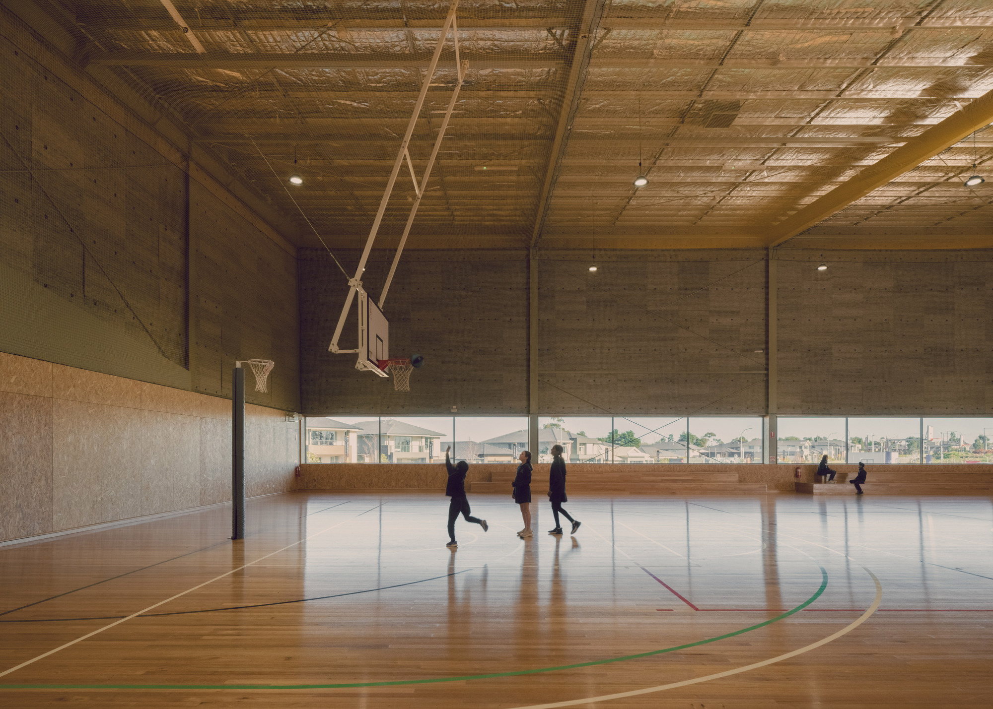 Interior basketball court with exposed timber plank ceiling, board-formed concrete walls and high clerestory glazing with students playing