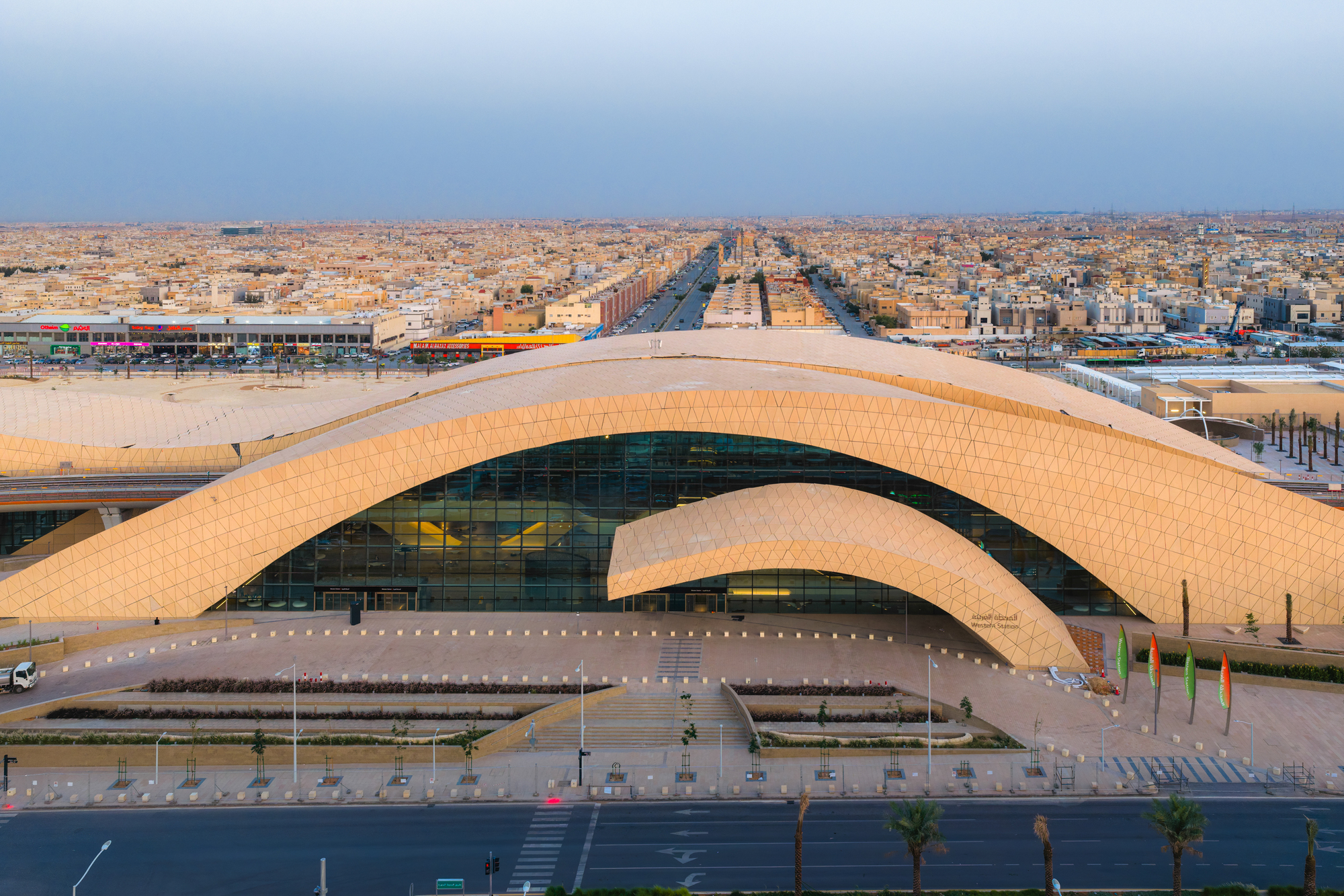 Aerial view of the arched tiled roof over glazed entrance plaza with palm-lined road in late afternoon light