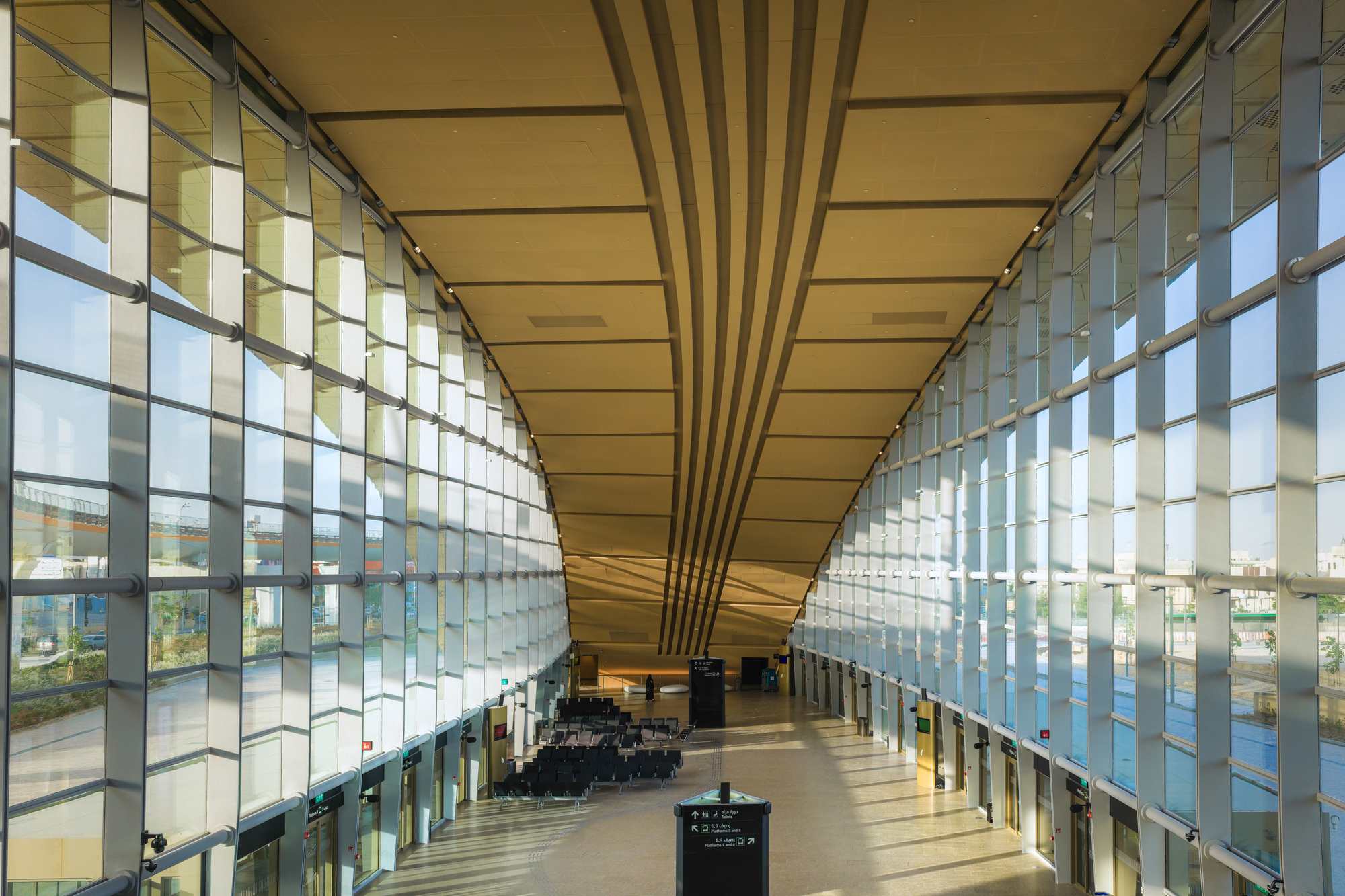 Symmetrical glass curtain walls flanking a central corridor with converging timber ceiling beams in daylight