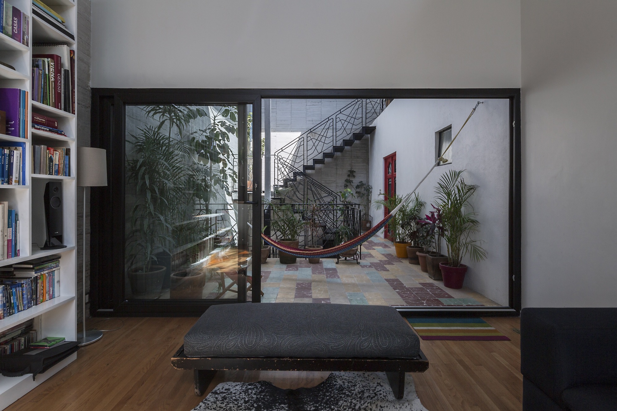 Living room seen through a sliding glass wall toward the courtyard stair, with a hammock and a bookshelf on the left