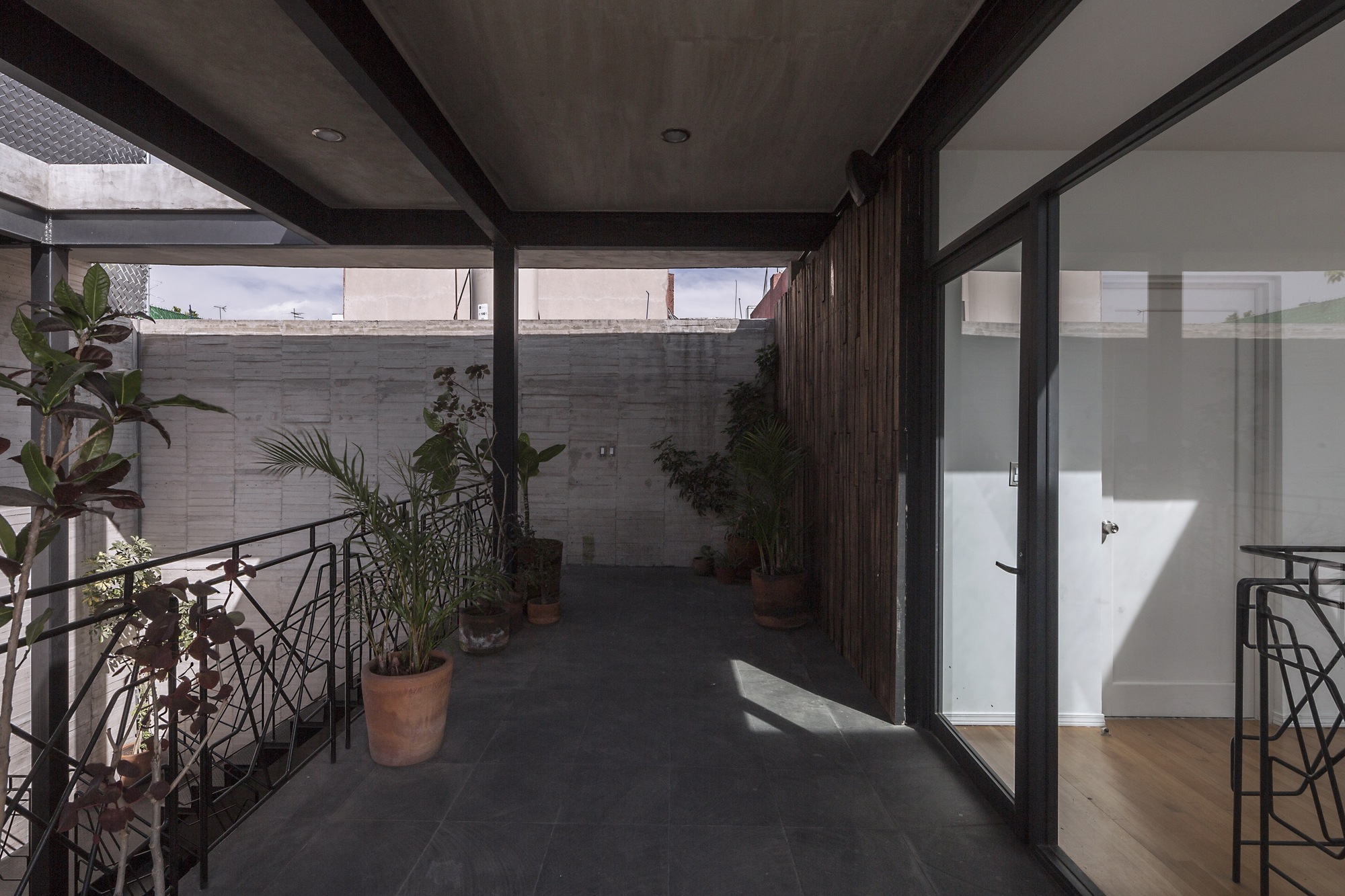 Covered upper walkway with dark slate floor, potted plants along the railing and a bamboo-clad wall beside sliding glass doors