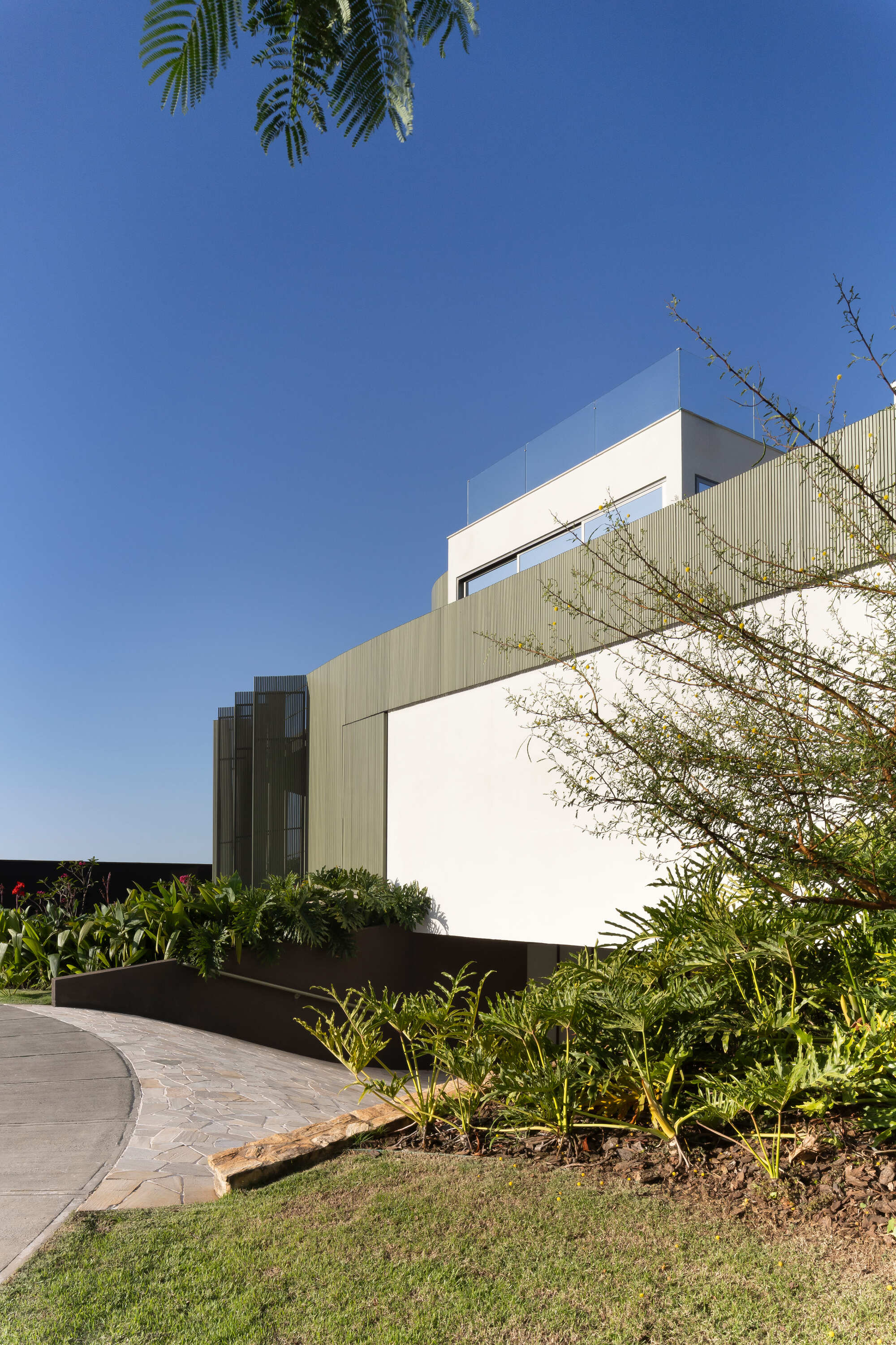 Layered exterior volumes with metal screening and planted beds along a curving paved path