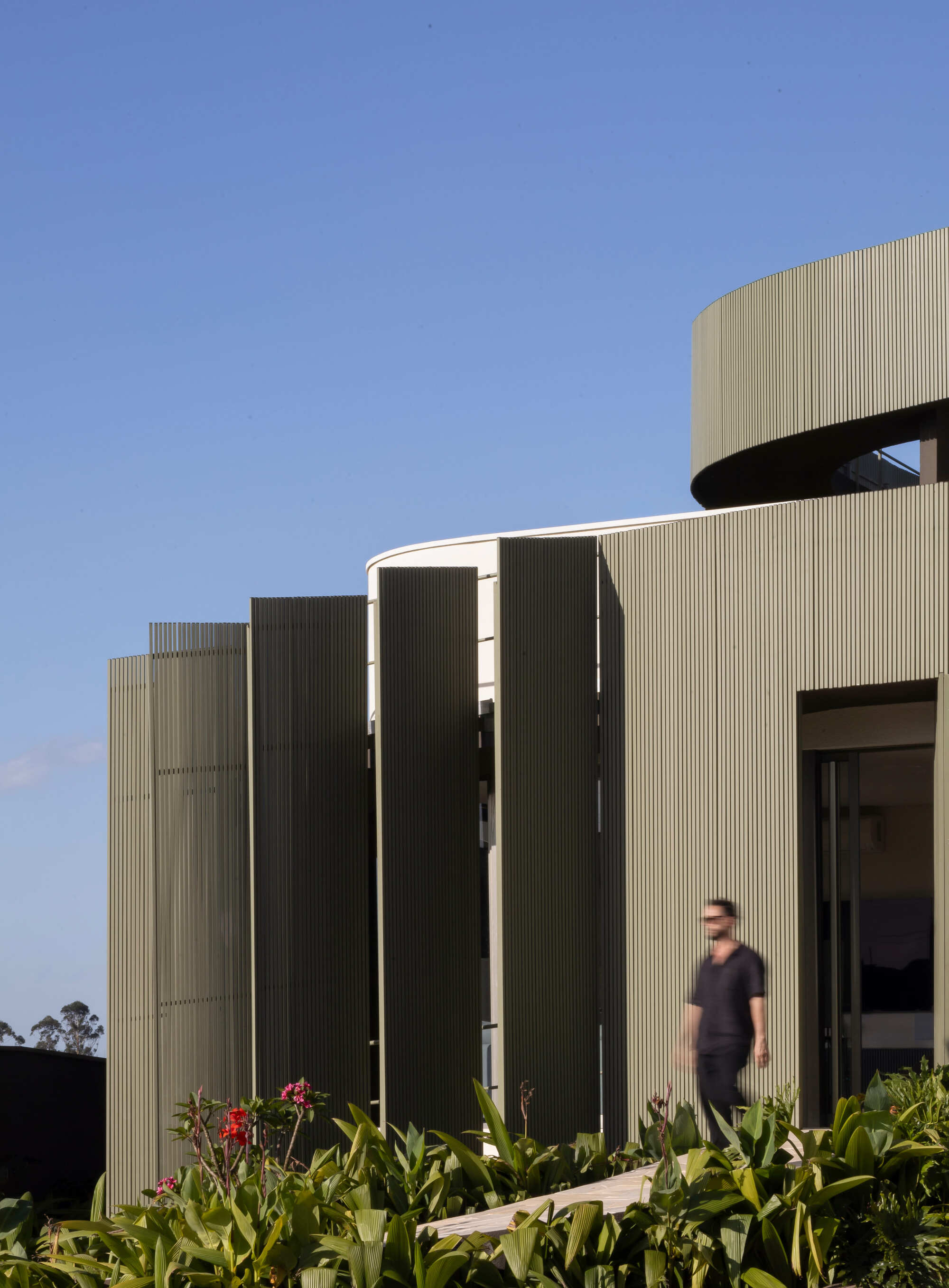 Vertical metal louvers screening the entrance with a figure passing through in afternoon light