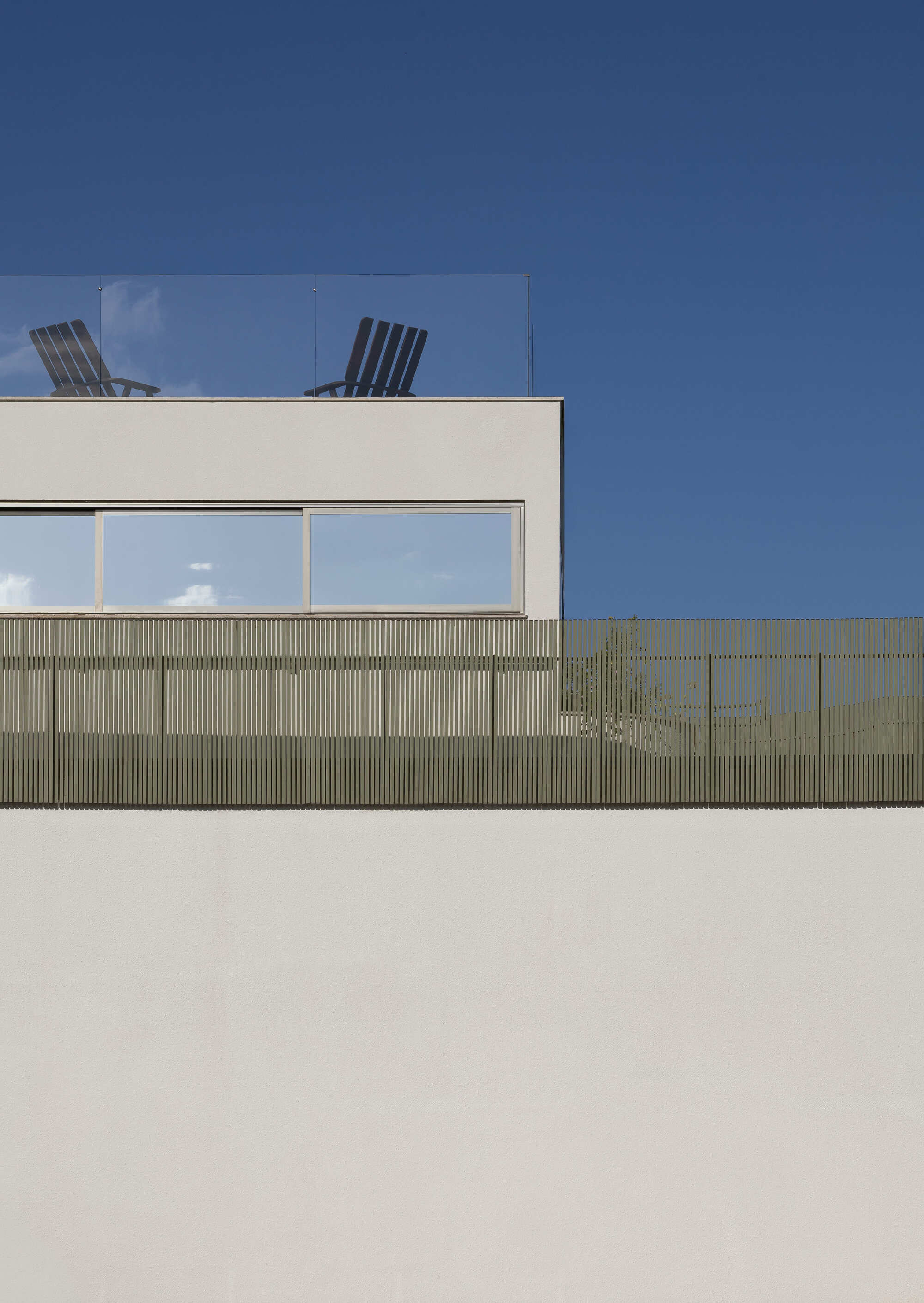 Upper level roof deck with glass balustrade, two lounge chairs and horizontal timber cladding below