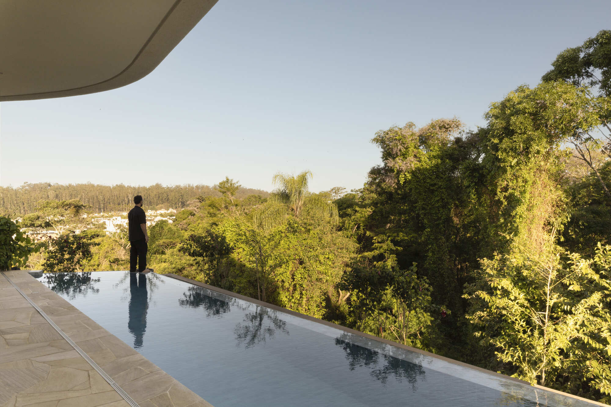 Infinity pool overlooking dense forest canopy with a figure standing at the edge