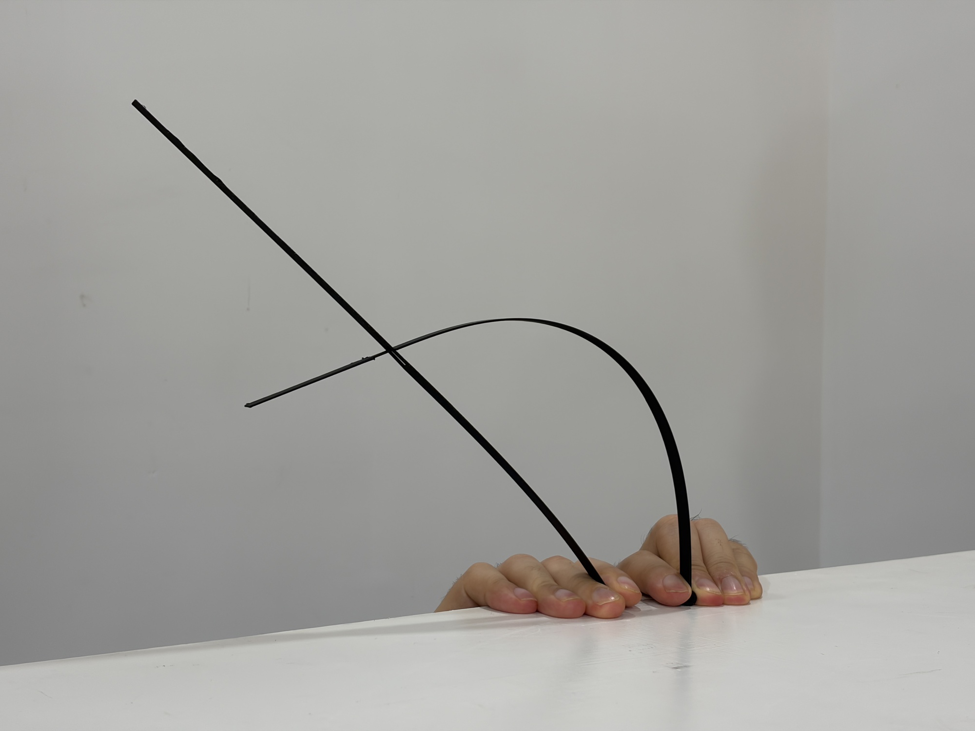 Close-up of a hand emerging from beneath a white surface holding bent metal rods