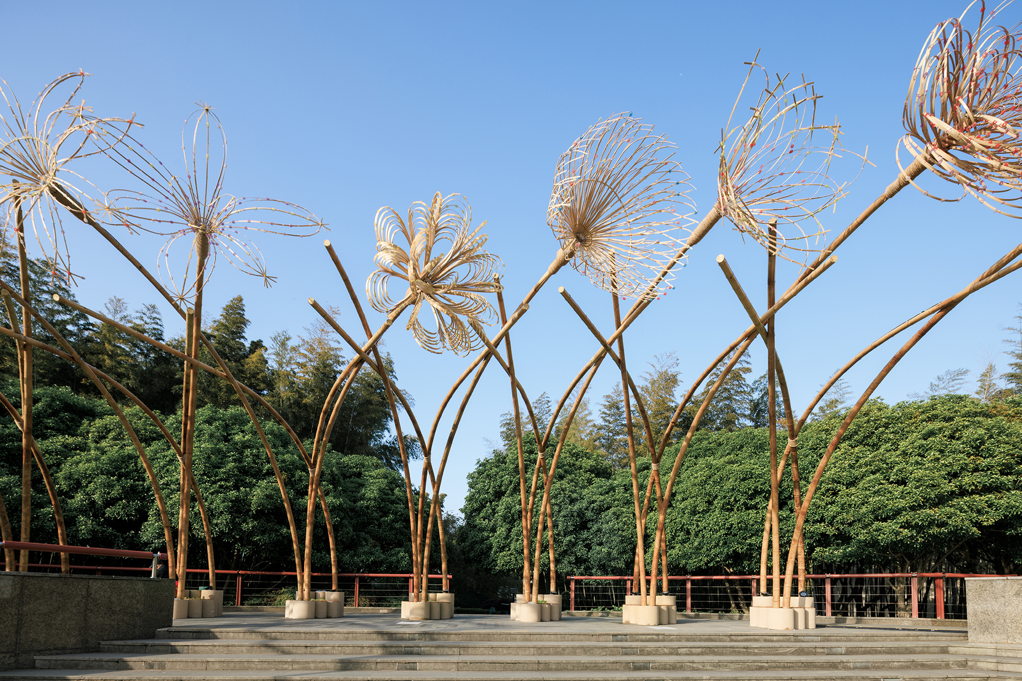 Sculptural bamboo installation with woven wire flower forms rising from concrete bases on stepped plaza